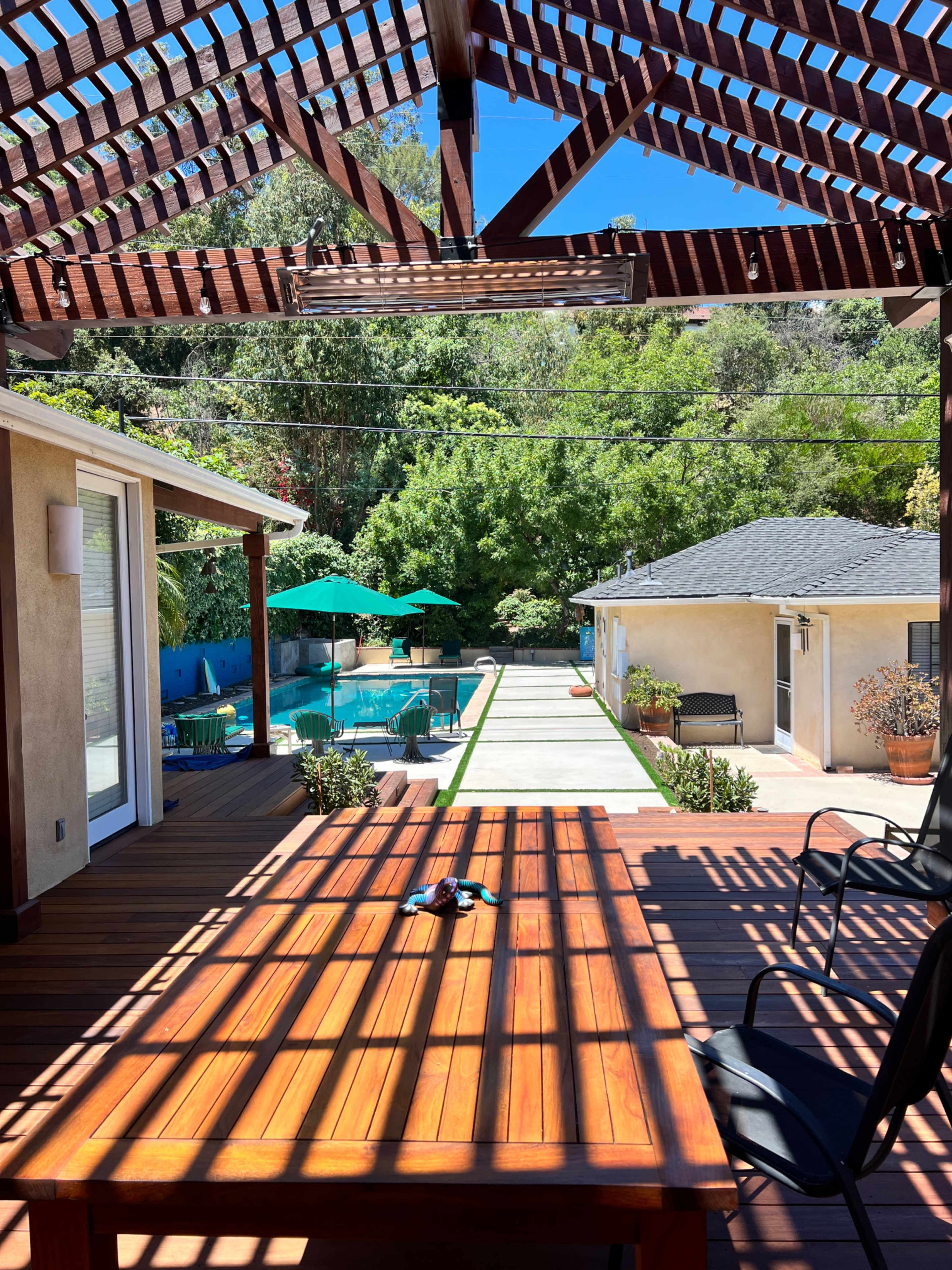 A wooden patio with a table and chairs, overlooking a landscaped area that includes a pool and green umbrellas.