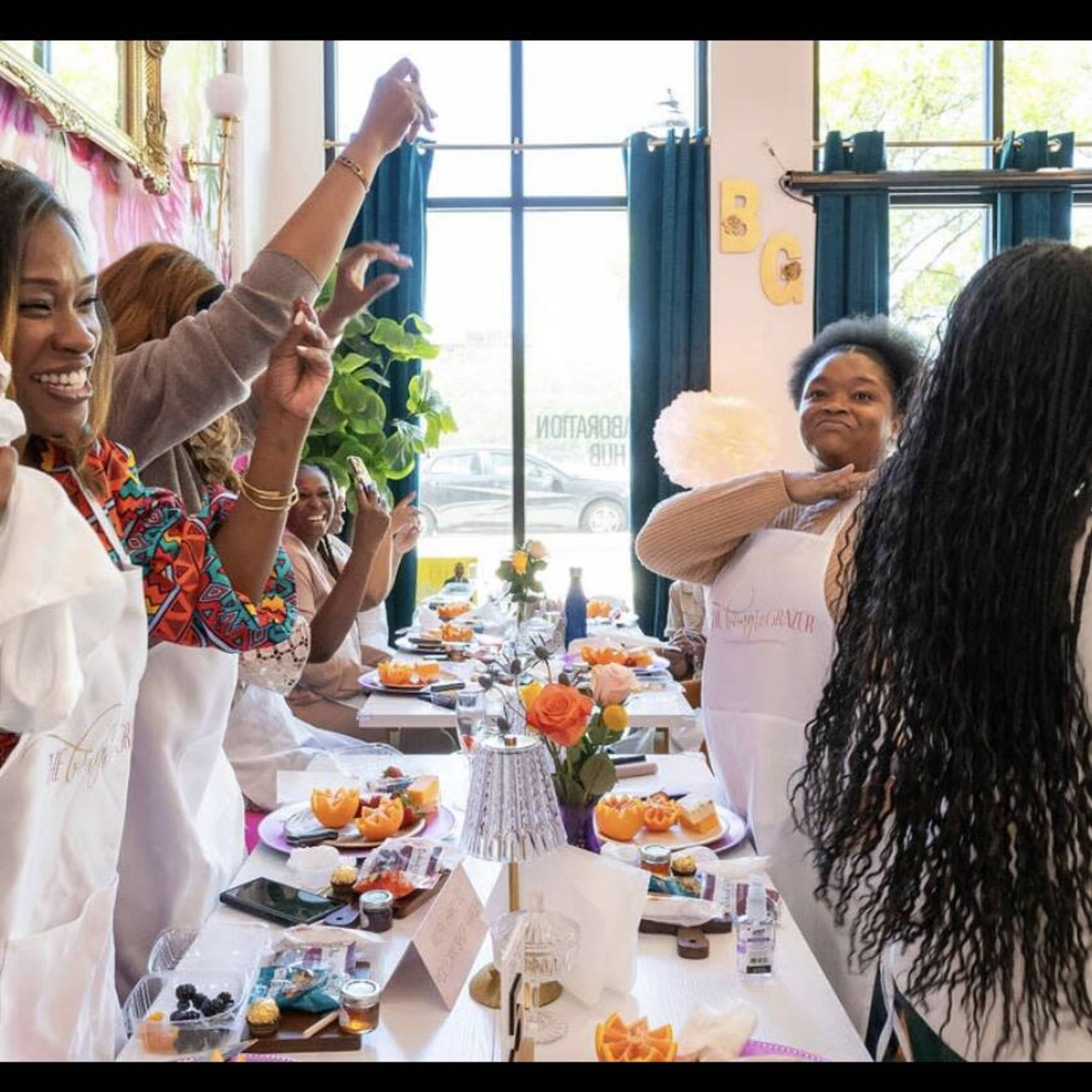 A group of women in aprons celebrates at a festive table adorned with food and decorations during a gathering.