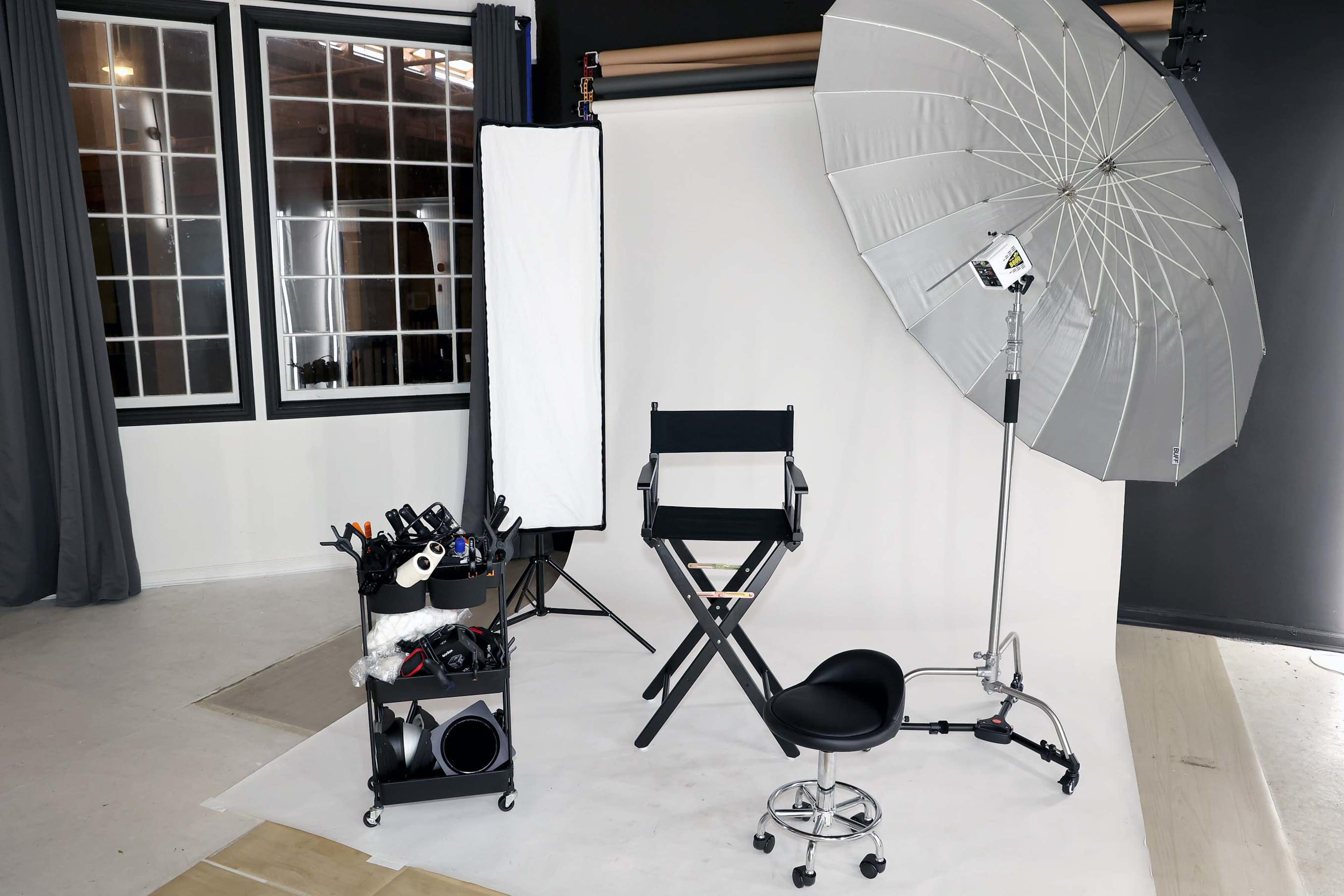 The image shows a photography studio setup with a makeup chair, lighting equipment, and various accessories on a cart against a backdrop.