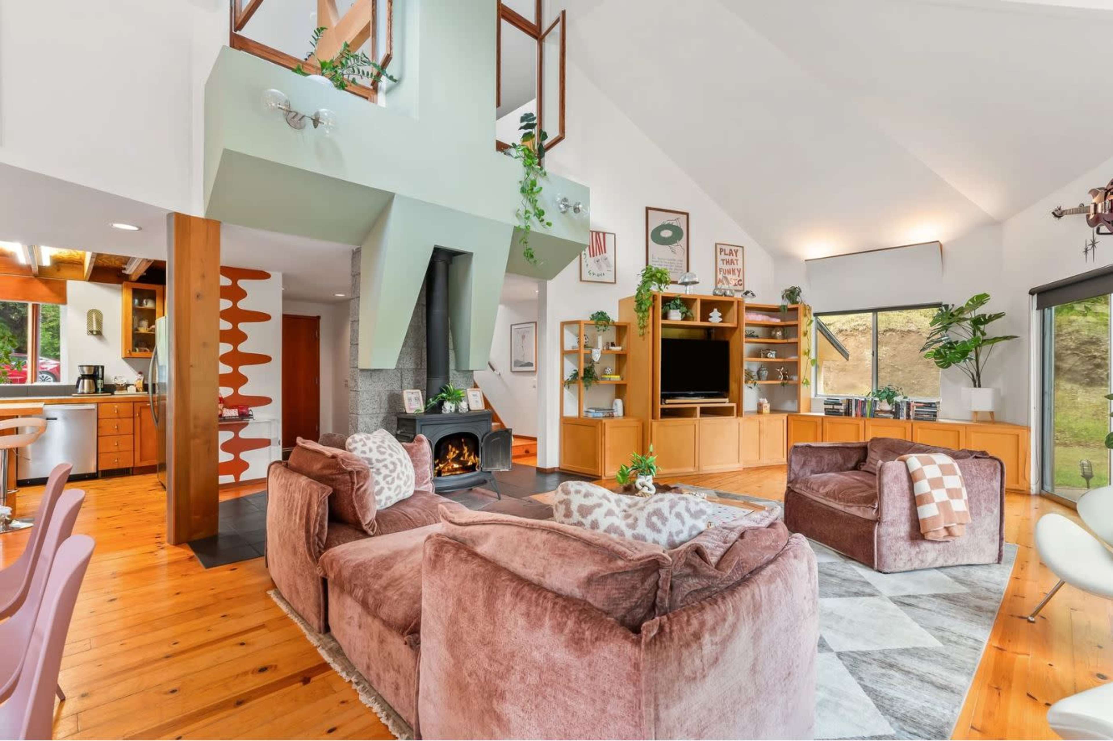 The image shows a spacious living area with a combination of a modern kitchen and a cozy seating arrangement, featuring large windows that provide natural light.
