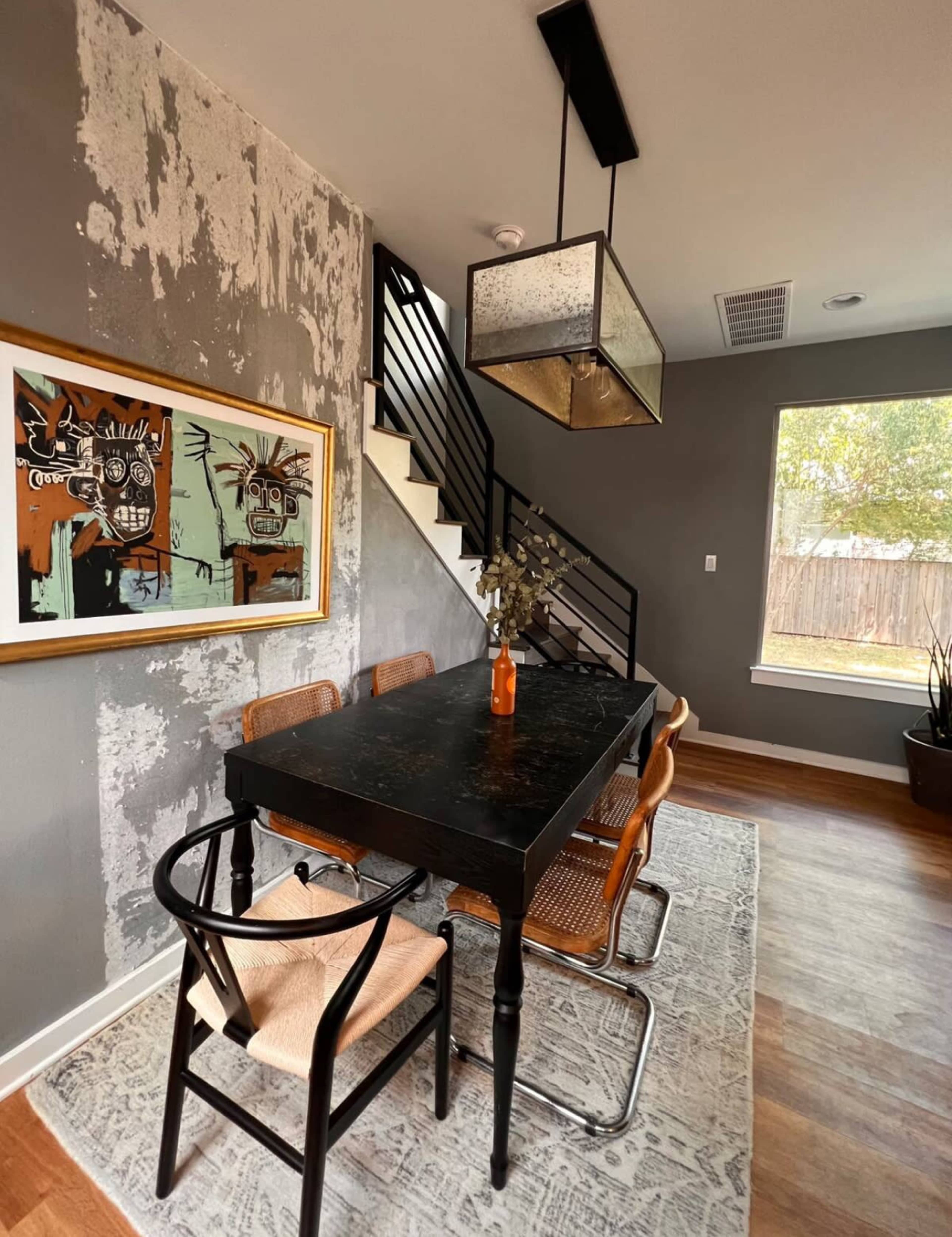 A dining area with a black table surrounded by chairs, a framed artwork on the wall, and a staircase nearby.