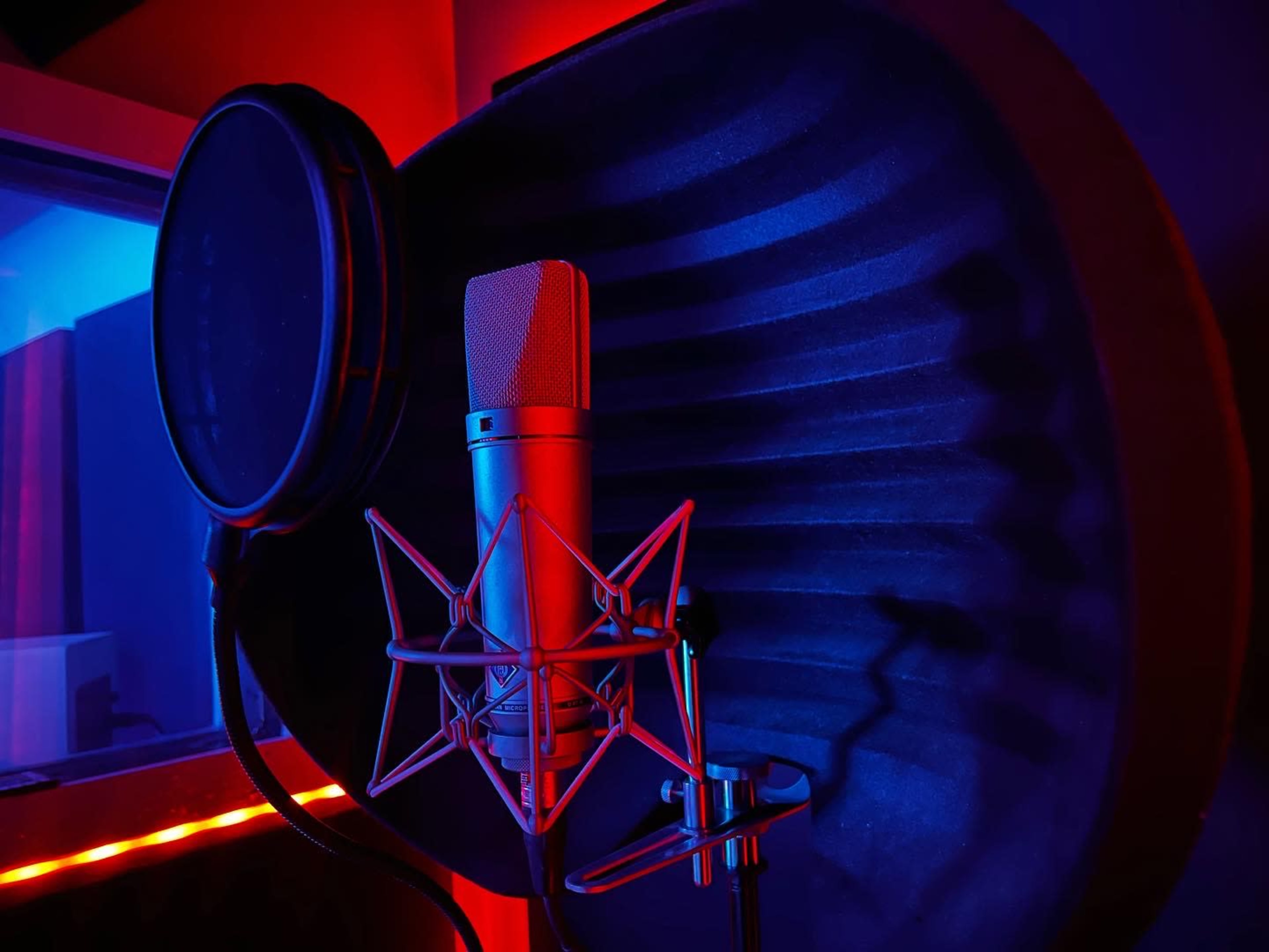 A microphone with a pop filter is positioned in front of a soundproof backdrop illuminated by blue and red lights.
