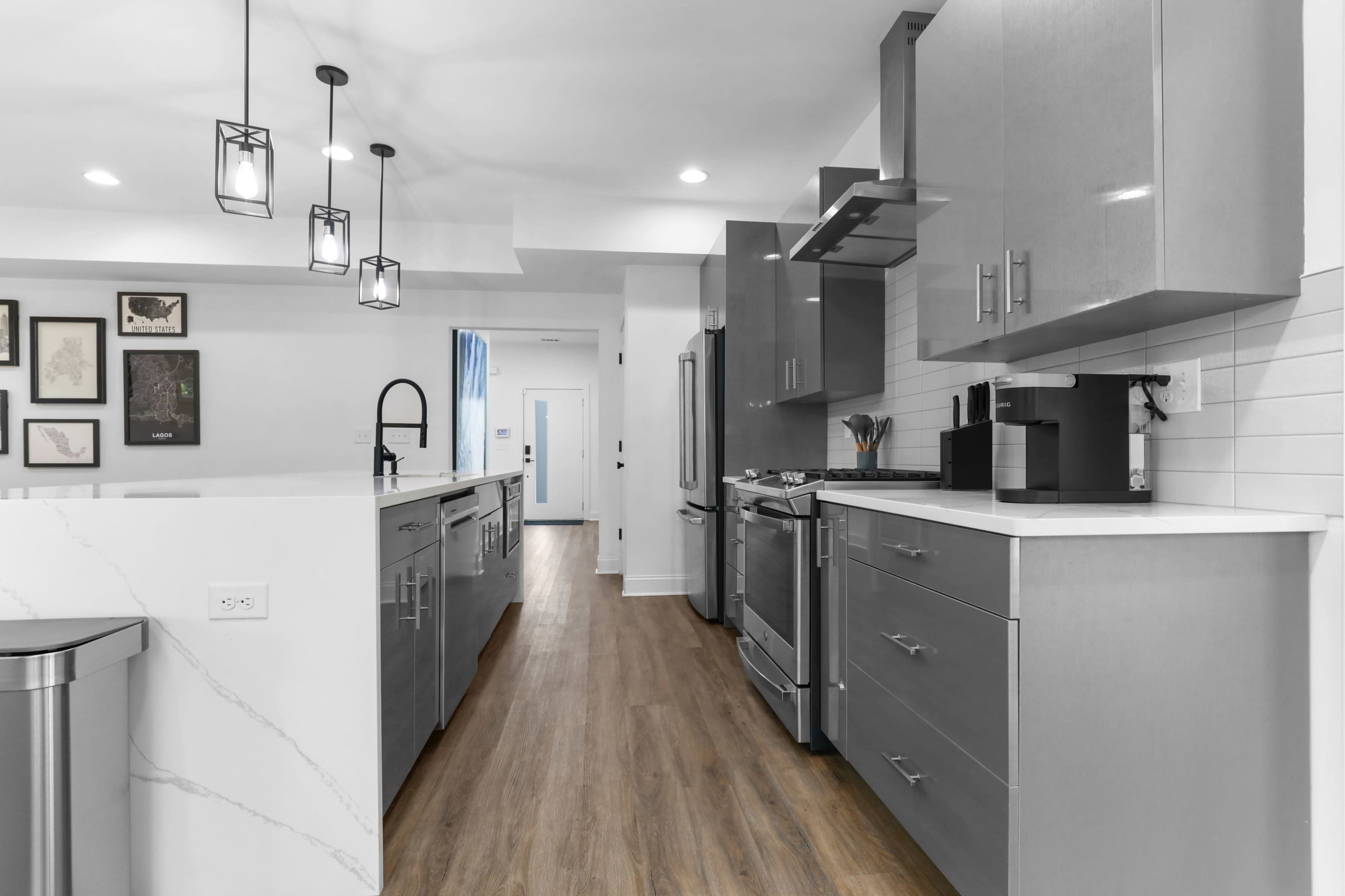 A modern kitchen features gray cabinets, stainless steel appliances, and a long, streamlined layout with wood flooring.