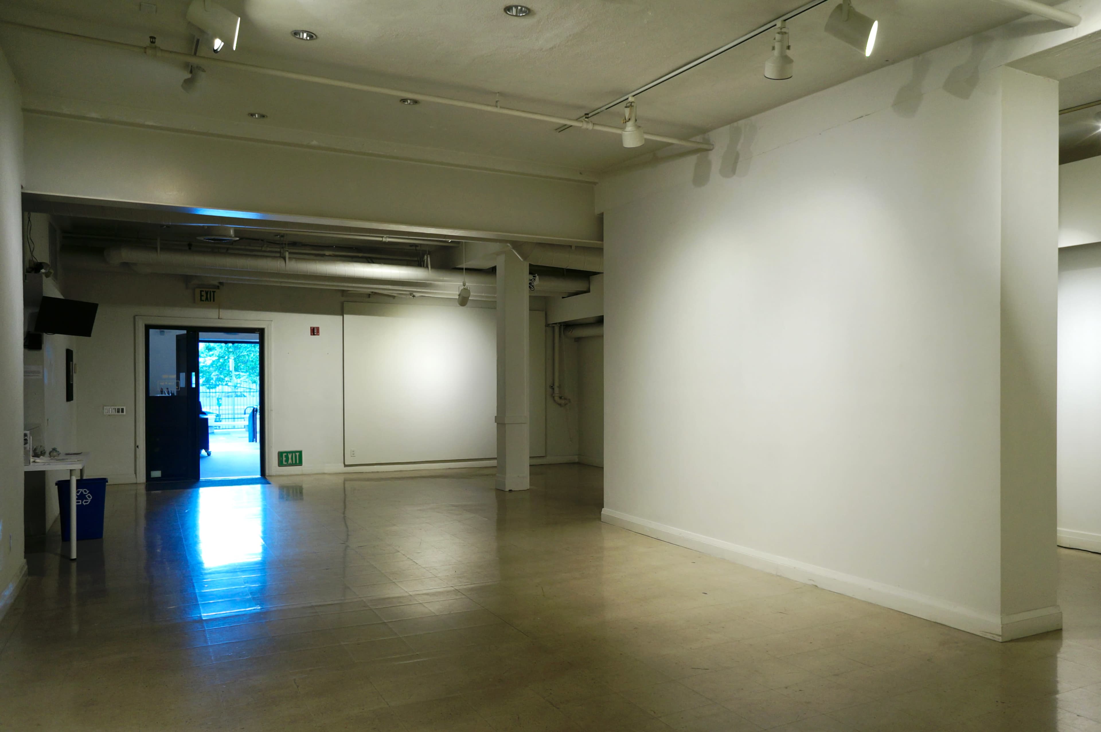 A spacious, empty art gallery with white walls and a door leading outside.