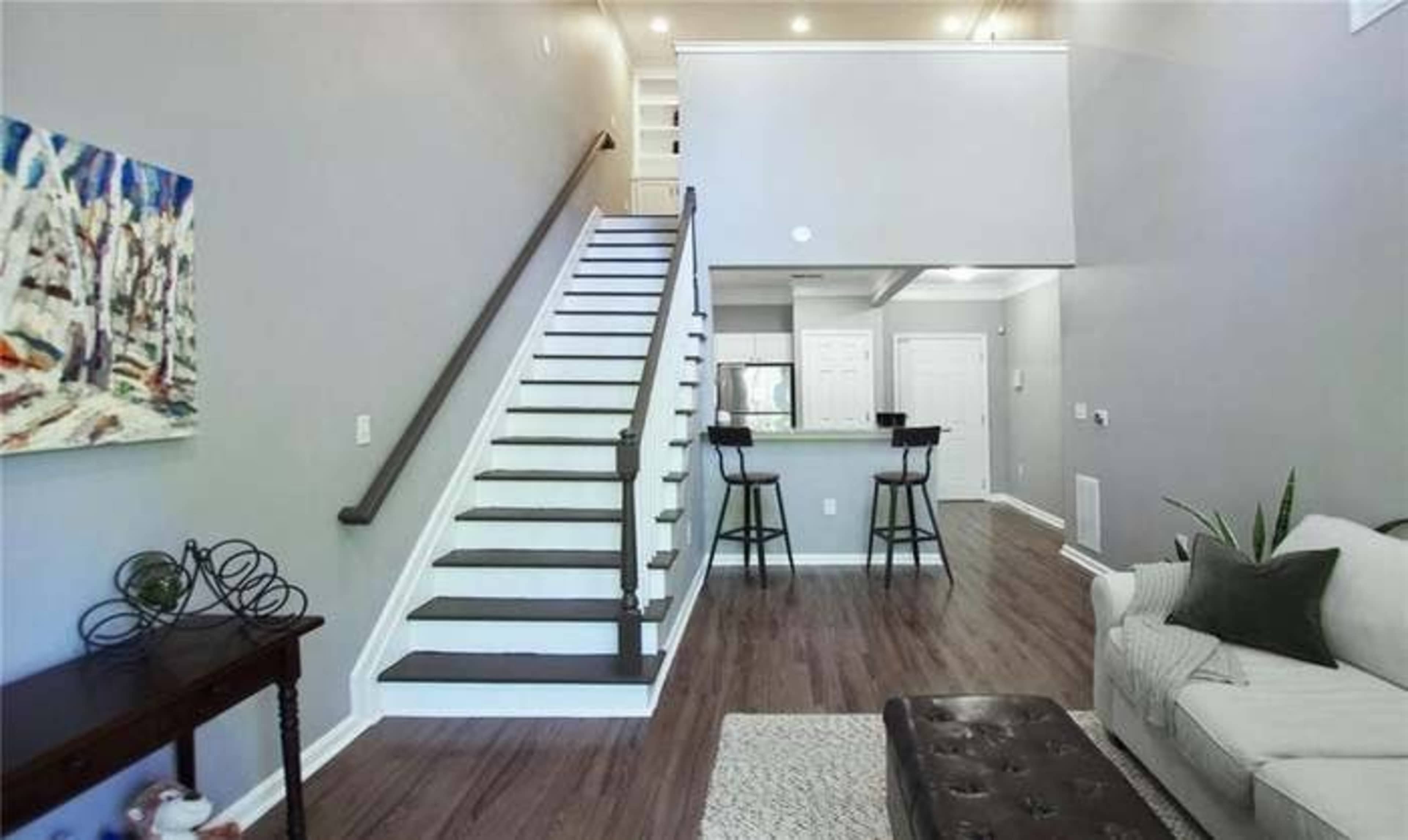 A modern living area with a staircase leading to an upper level, a sofa, and a small dining area in the background.