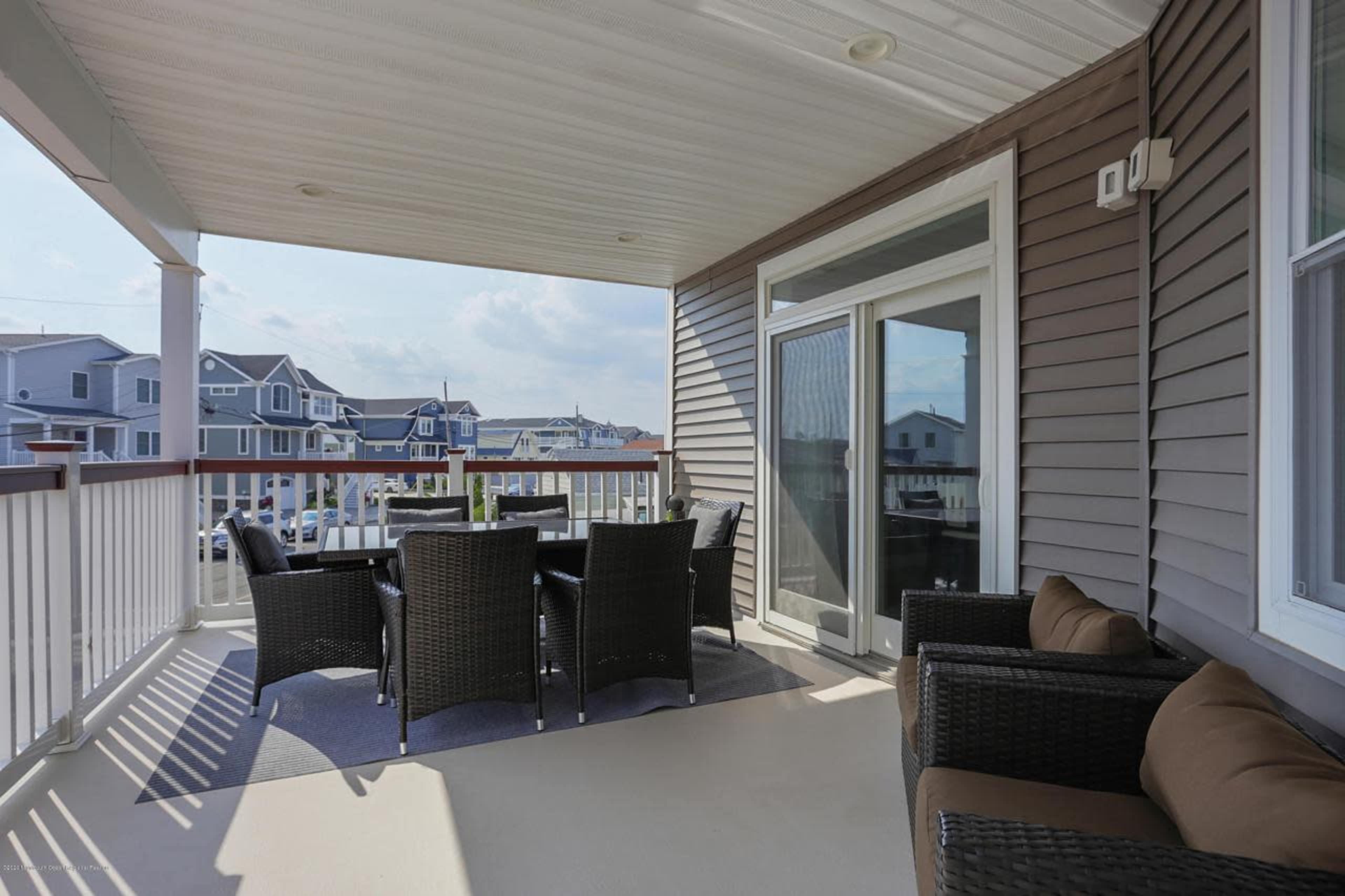 A spacious balcony with a dining table and chairs, surrounded by a railing and overlooking nearby houses.