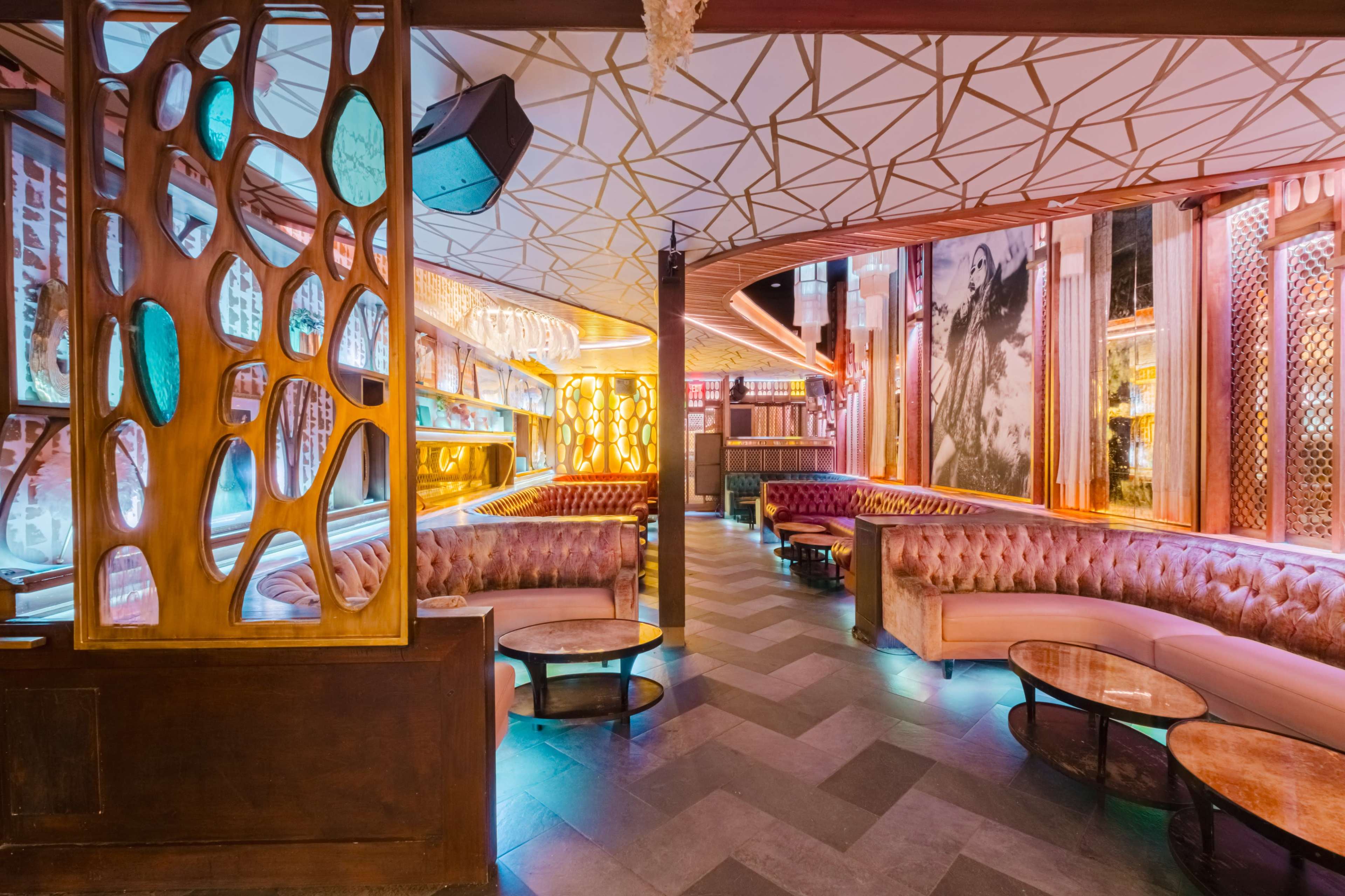 The image shows a modern lounge bar with illuminated decor, curved seating, and a vibrant atmosphere.