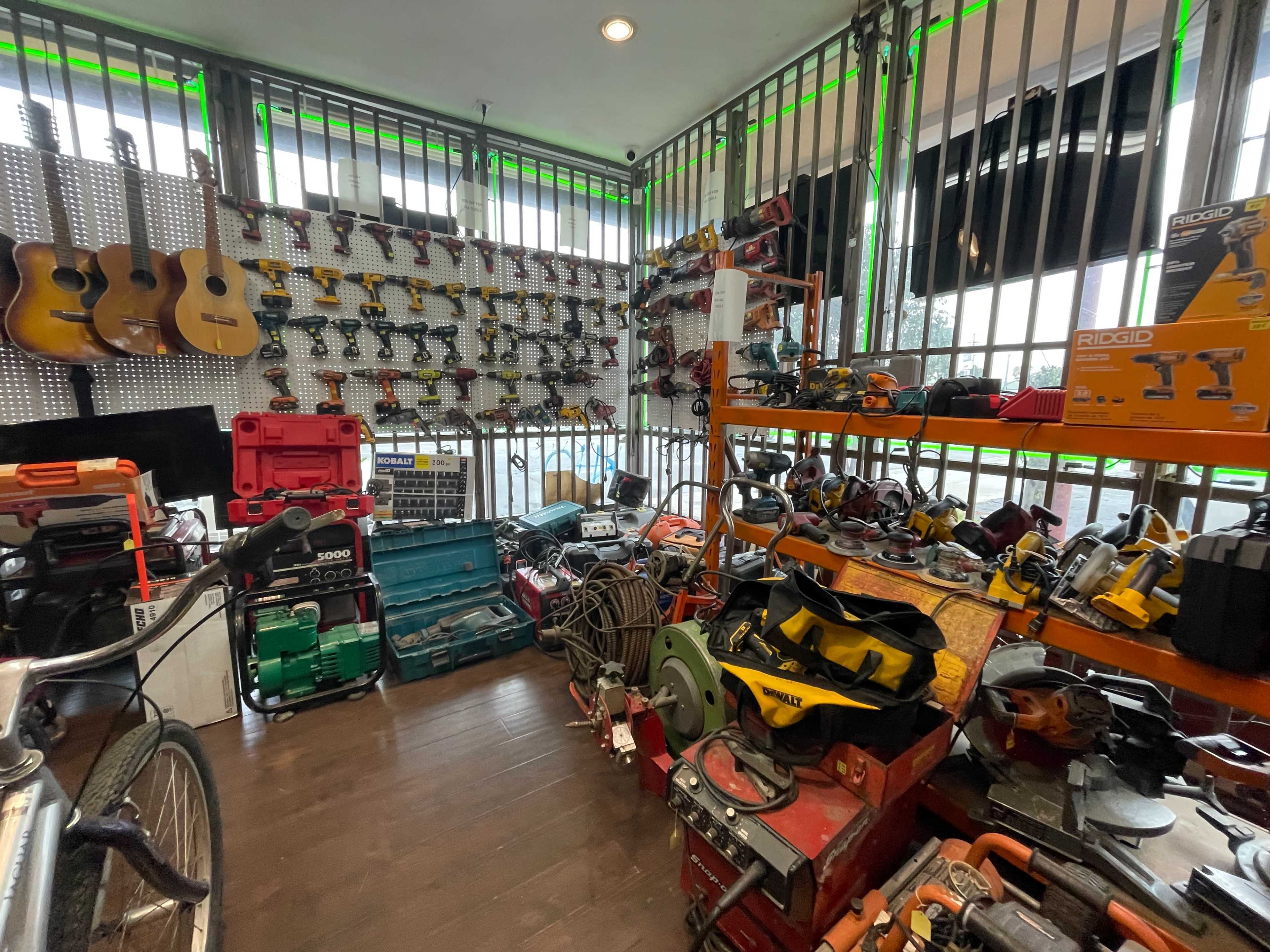 The image shows a tool shop with various power tools, hand tools, and musical instruments arranged on shelves and tables, enclosed by metal bars.