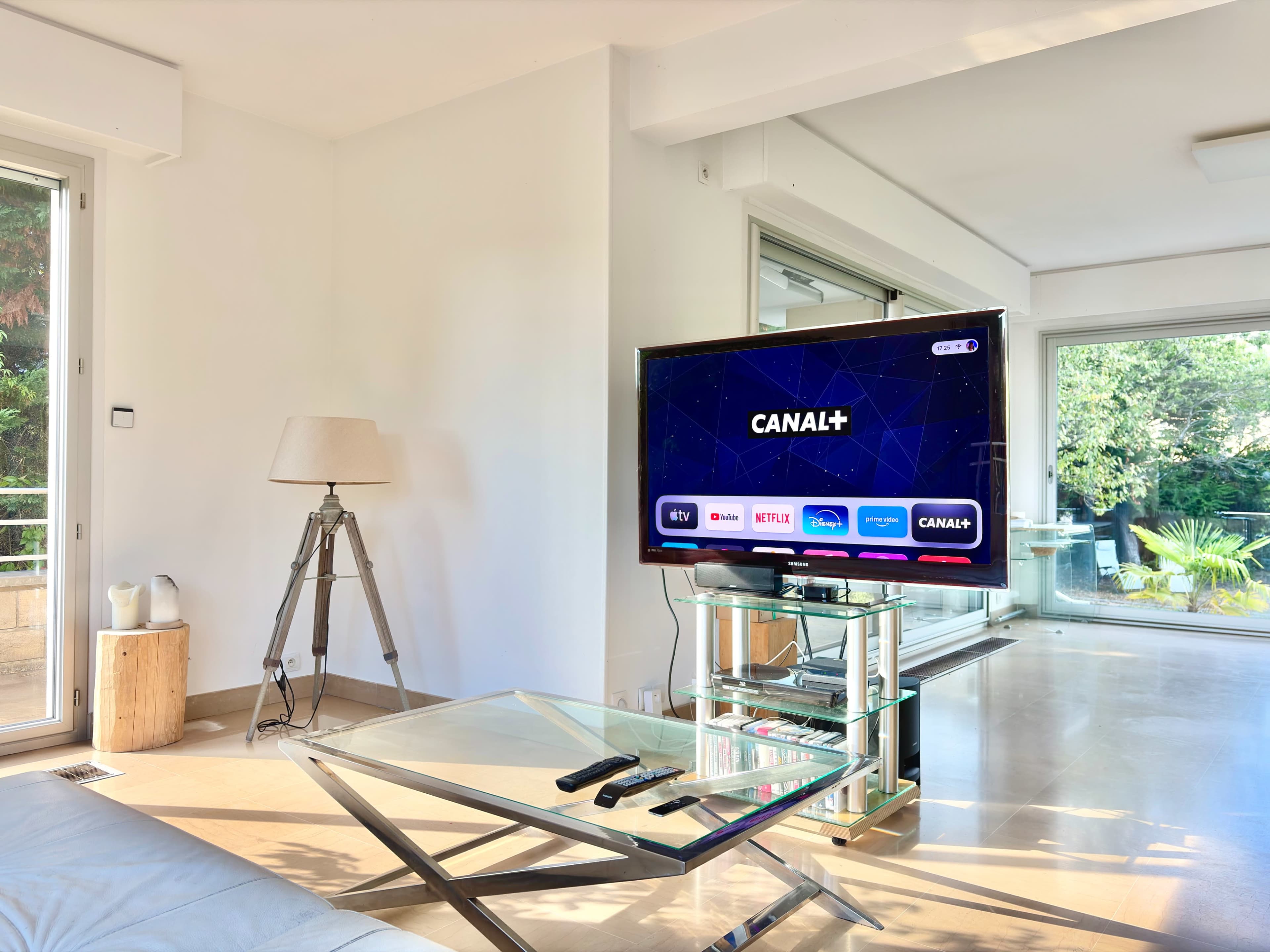 A modern living room features a television displaying streaming service options, with a lamp and glass coffee table in the foreground.