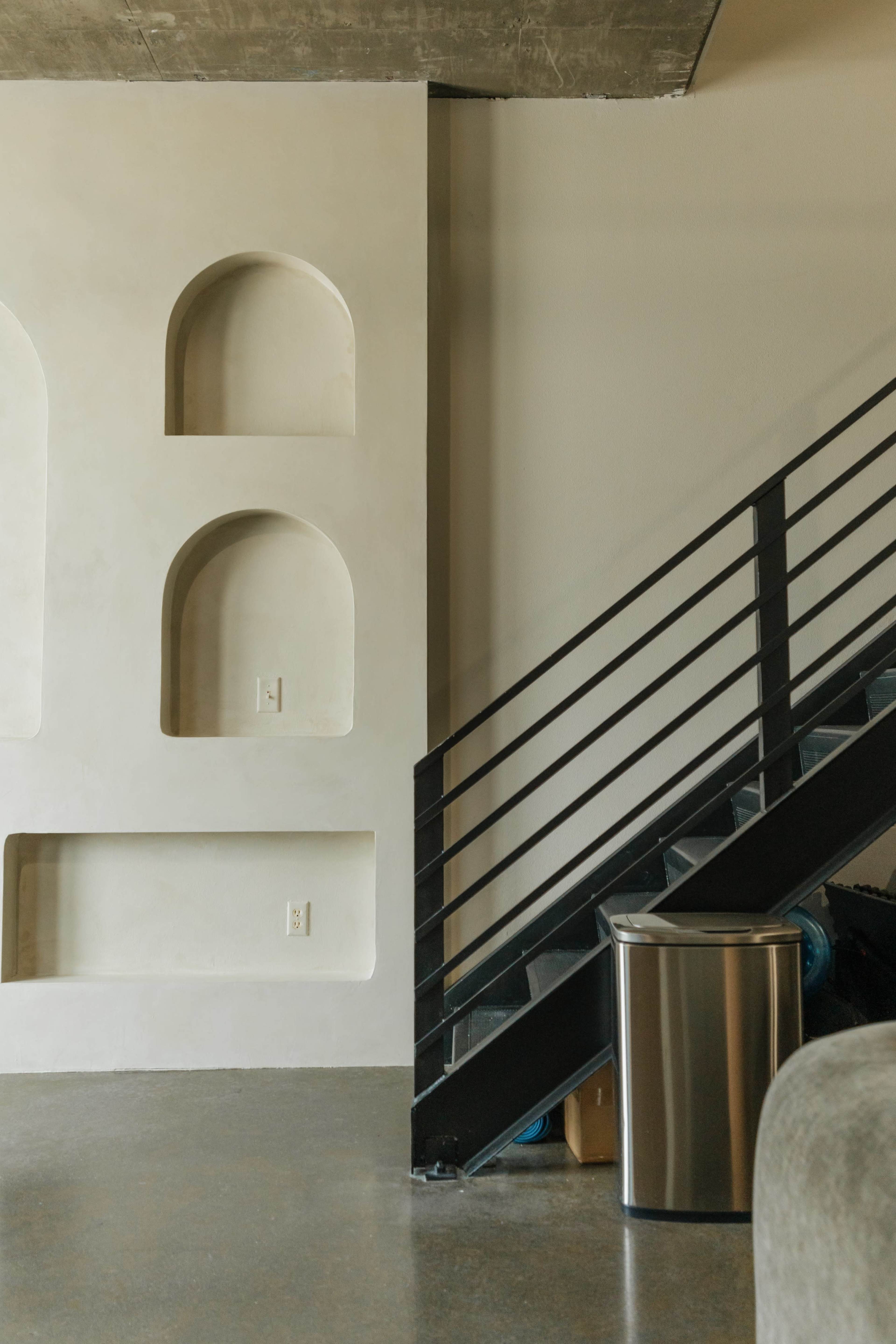 A metal staircase leads up alongside a wall featuring built-in niches and a trash can at the base.