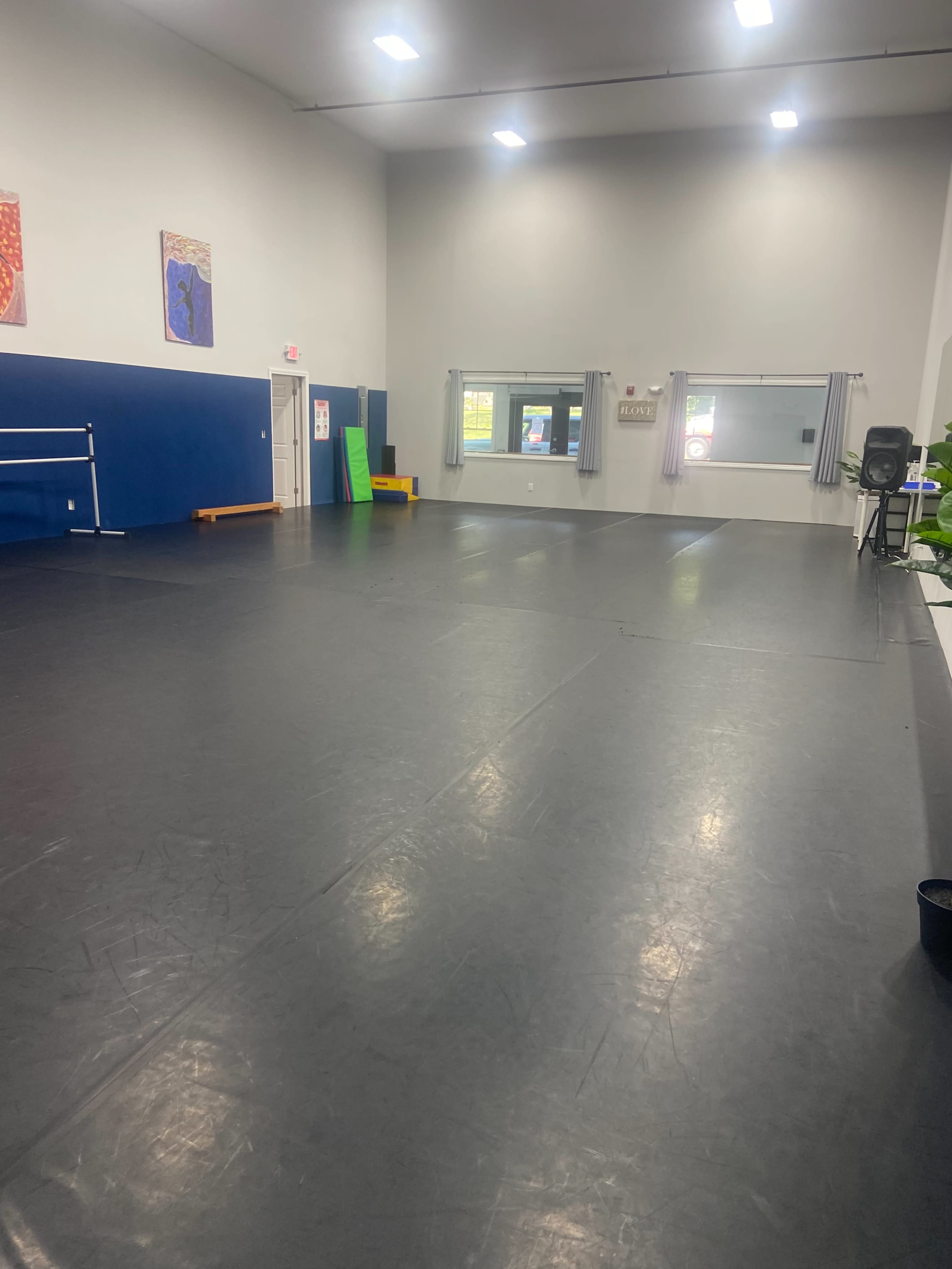 The image shows a spacious dance studio with a polished black floor, mirrors on one wall, and various exercise equipment along the sides.