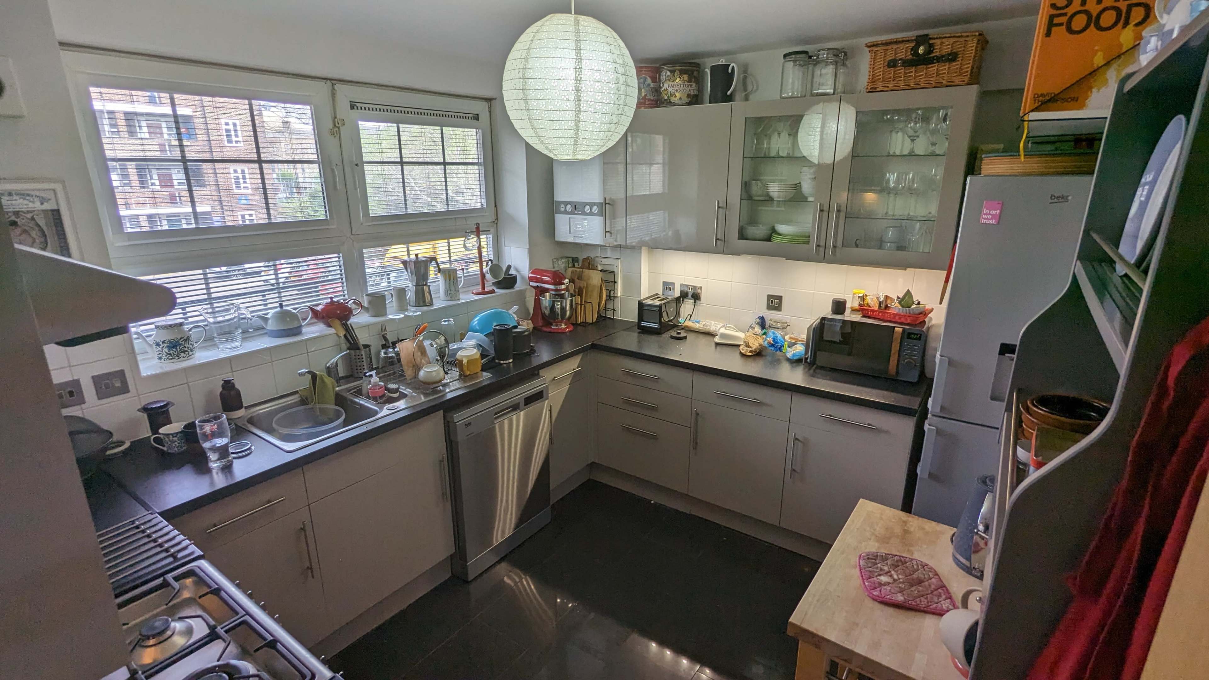 The image shows a modern kitchen with grey cabinets, a black countertop, and various appliances arranged along the walls.