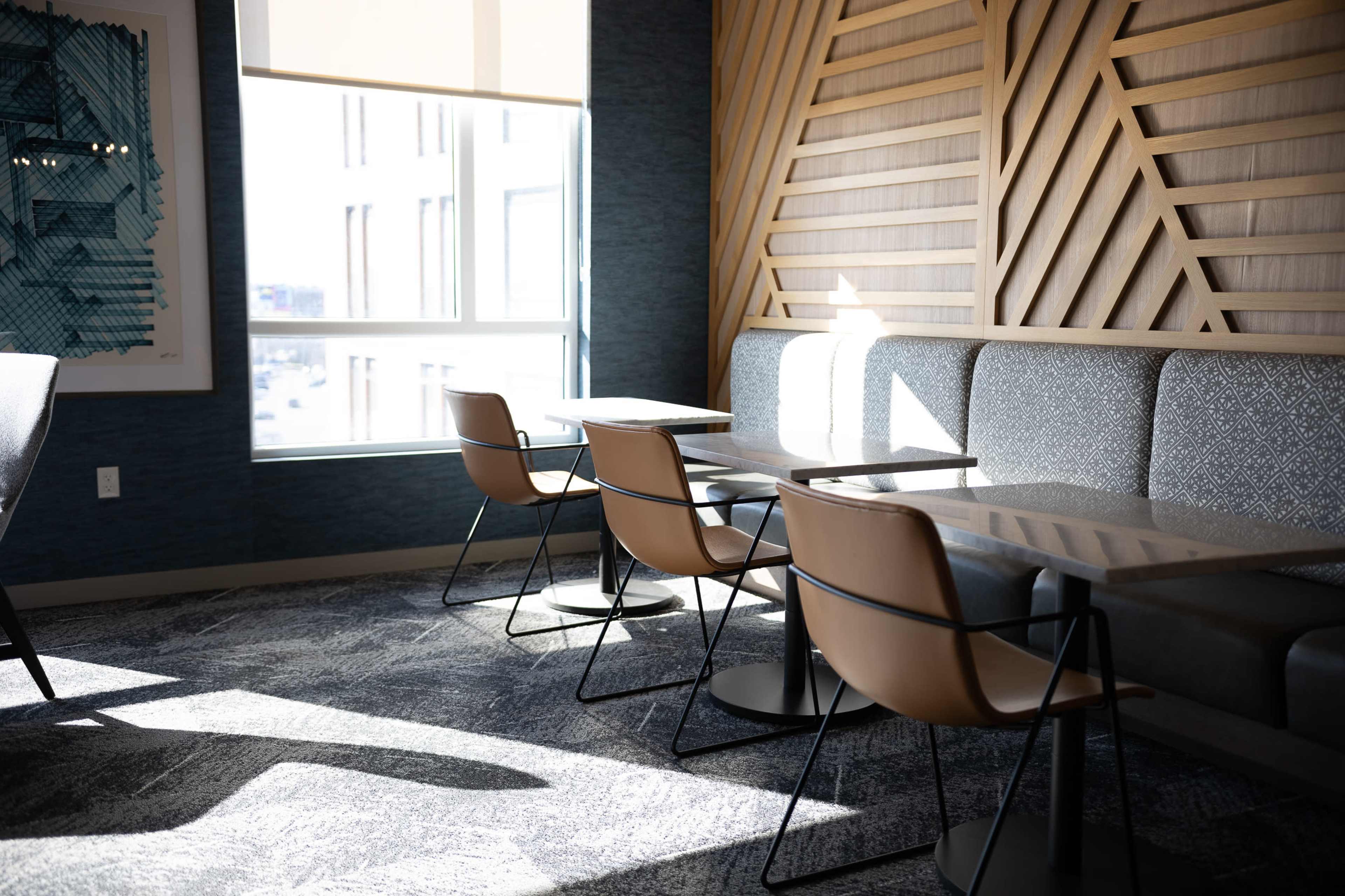 The image shows a well-lit seating area with wooden paneling, featuring two tables and four chairs against a window.