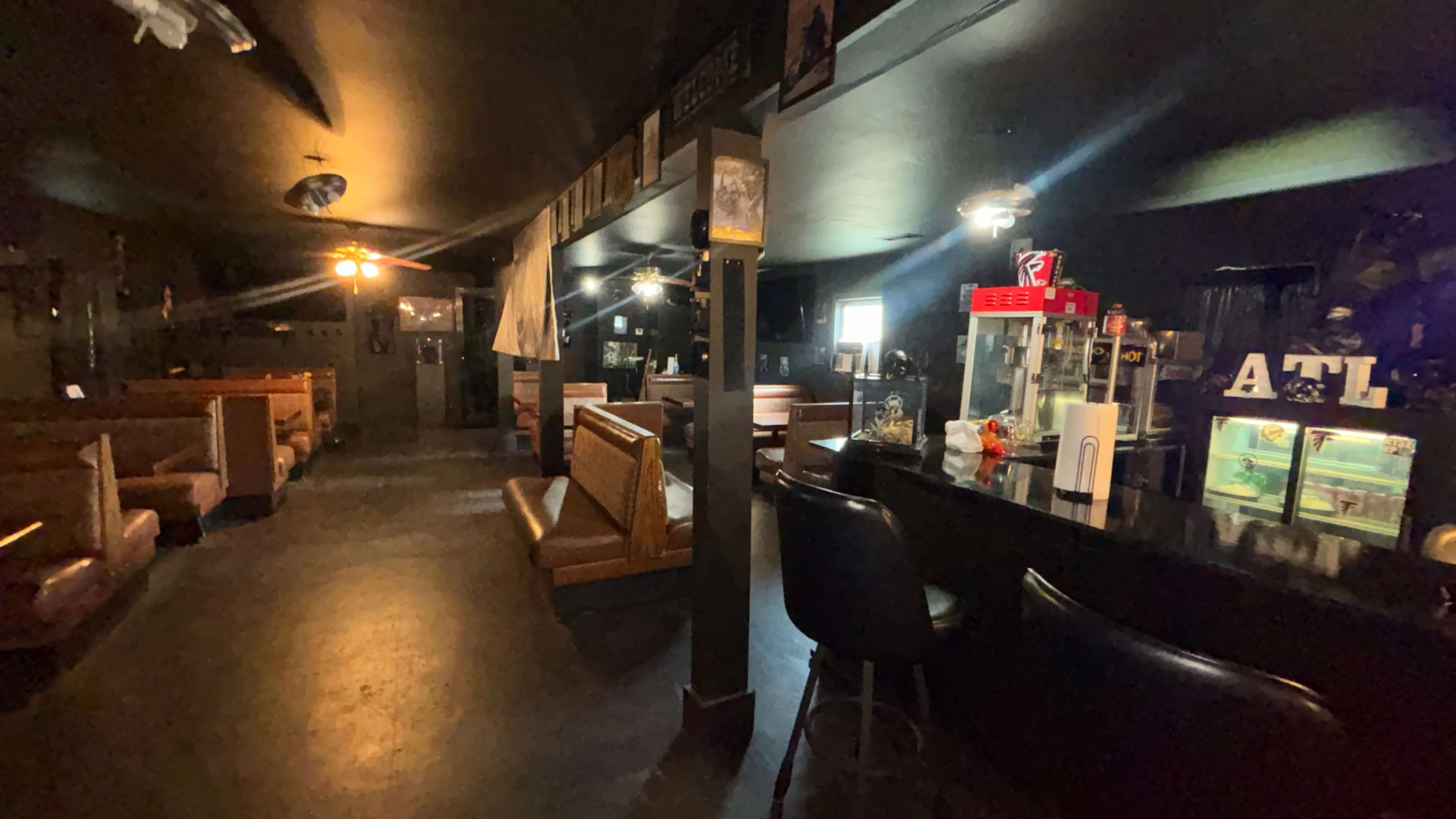The dimly lit interior of a bar features a long counter, a few booths, and decorative items on the walls.
