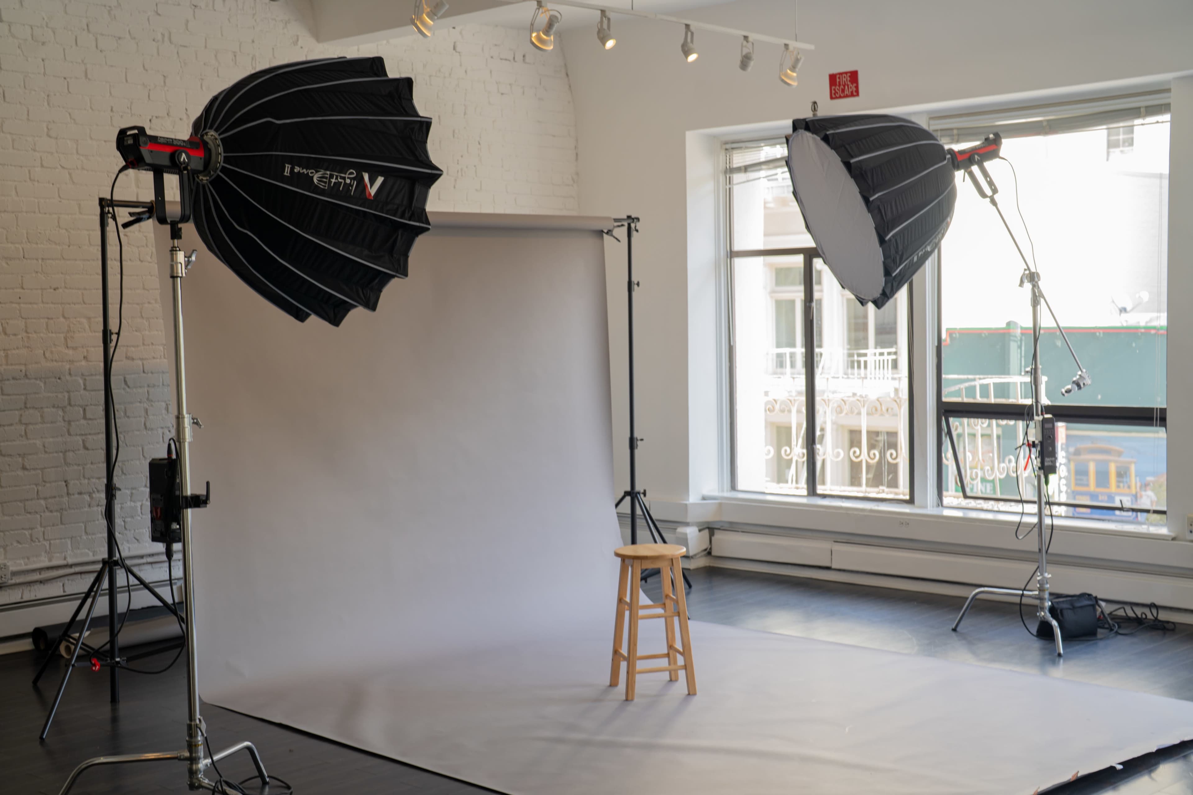 A photography studio setup with two softbox lights and a blank backdrop, featuring a stool positioned in front of it.