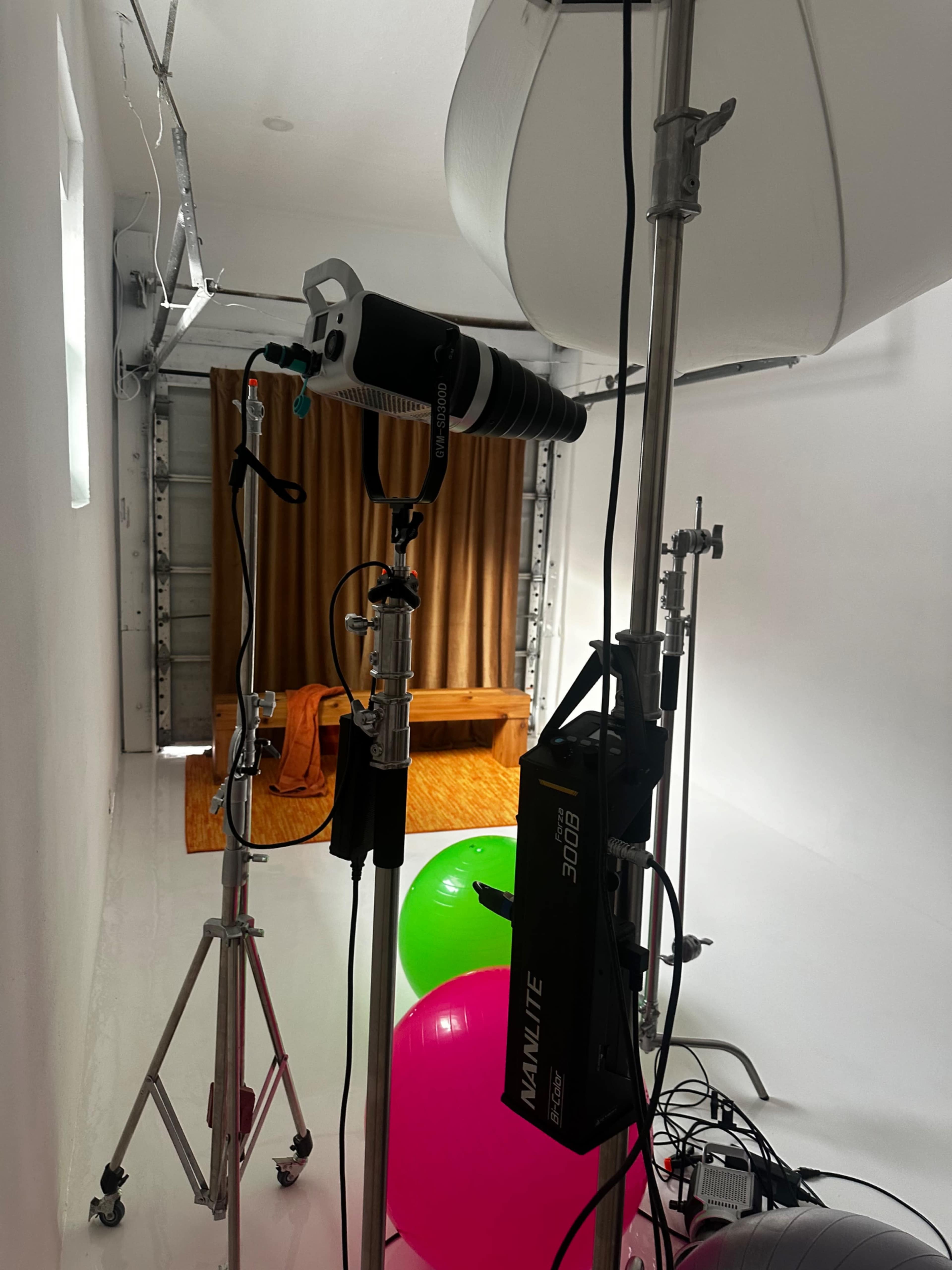 A photography setup in a white room with a light stand, a softbox, and colorful balloons in the foreground.
