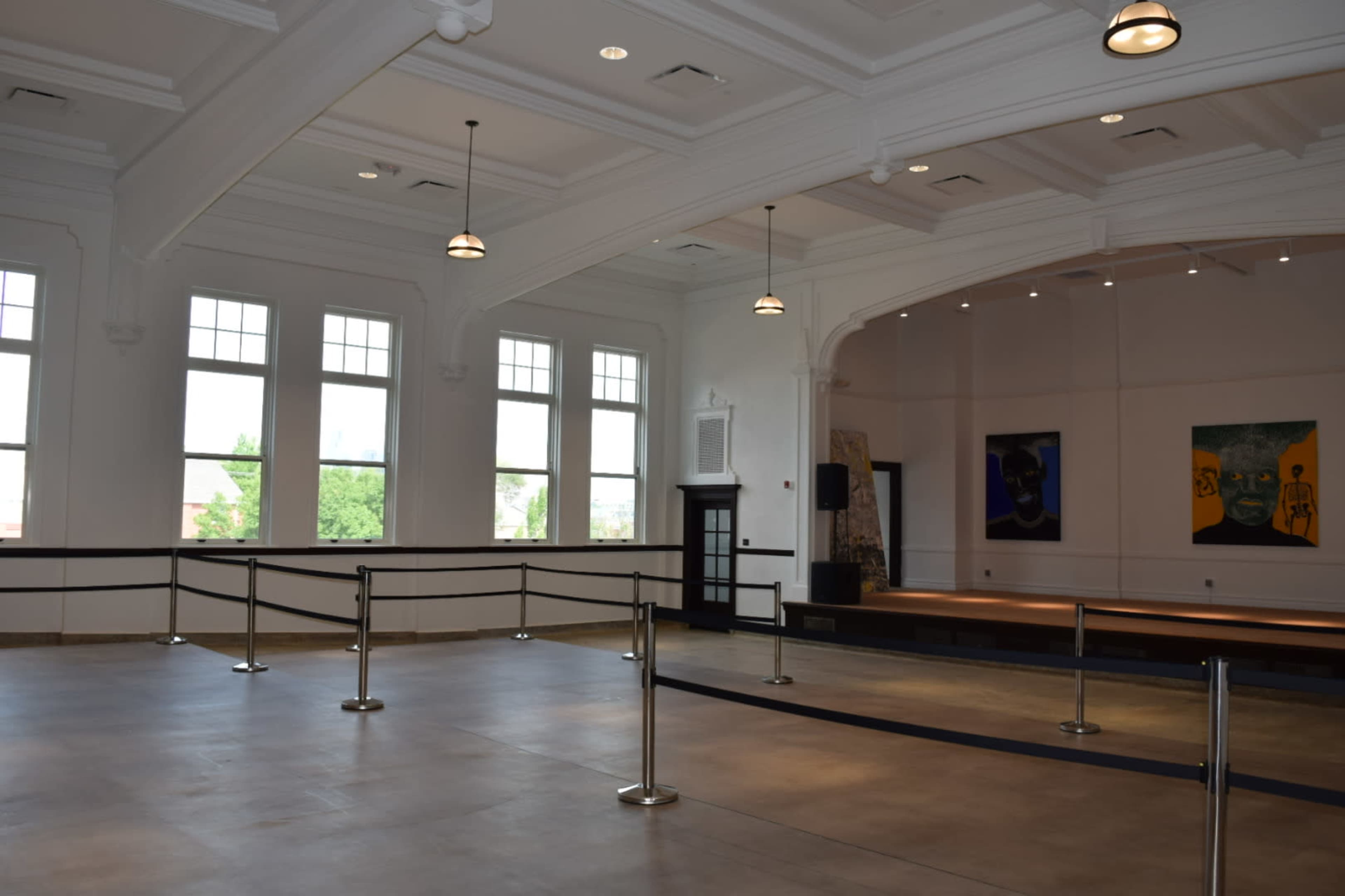 The image shows an empty hall with high ceilings, large windows, and barriers separating the space.