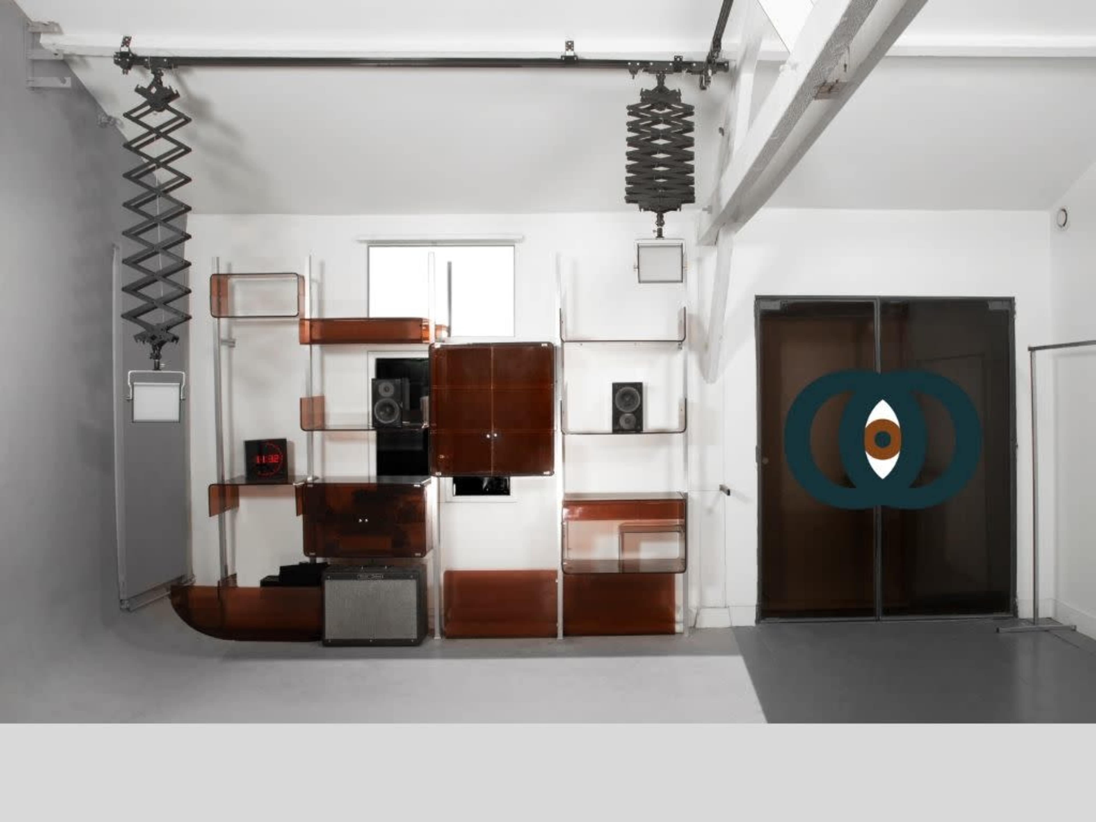 The image depicts a modern interior space featuring a clear shelving unit with various audio equipment and speakers mounted on a white wall.