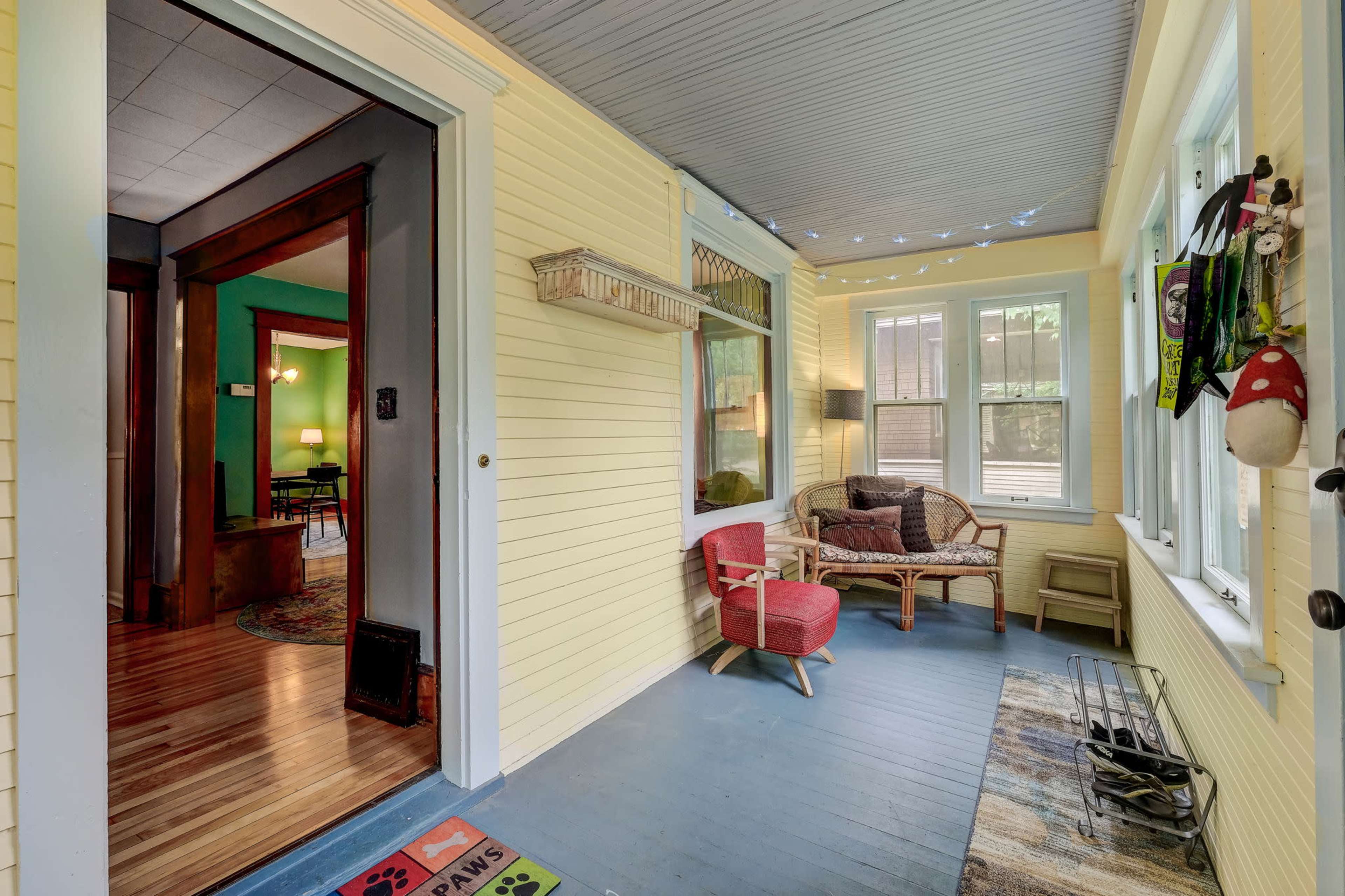 A brightly painted yellow porch with a wooden floor, featuring a cozy seating area, windows allowing natural light, and decorative elements like a welcome mat and hanging items.