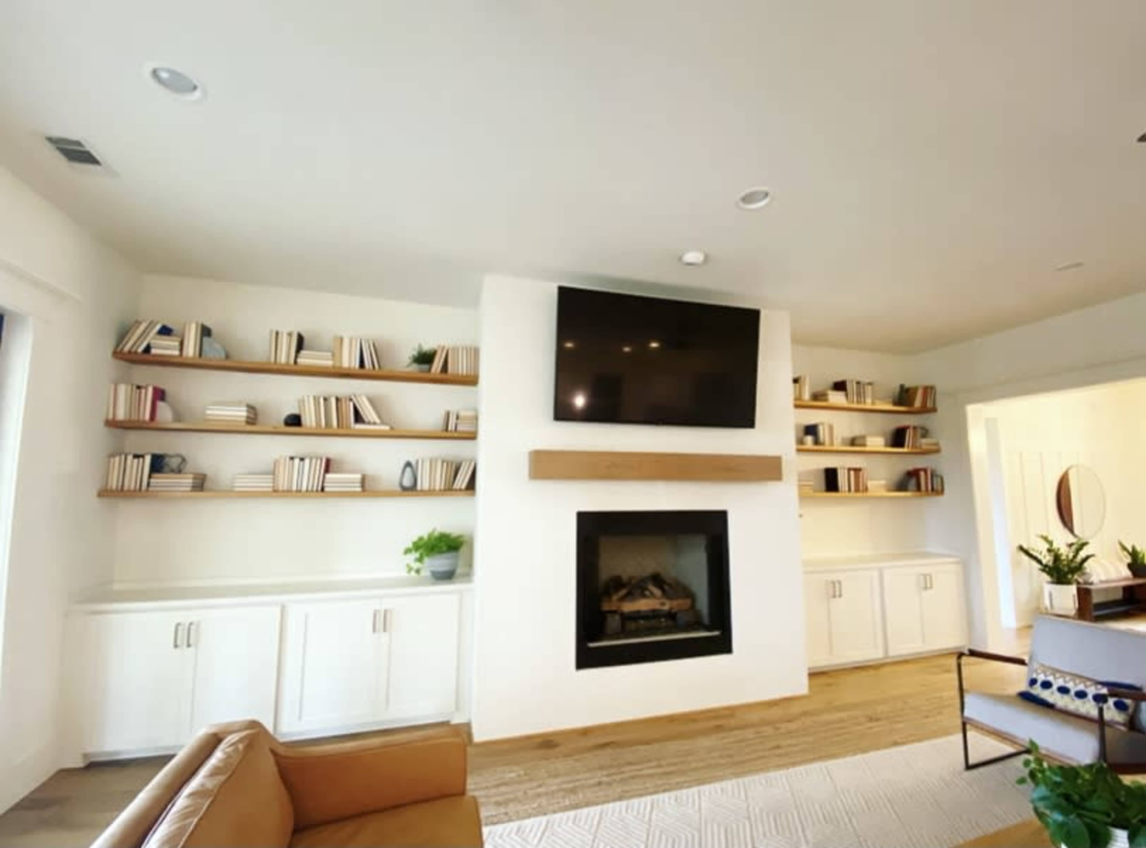 A living room features a fireplace with a television mounted above it and built-in shelves filled with books on either side.