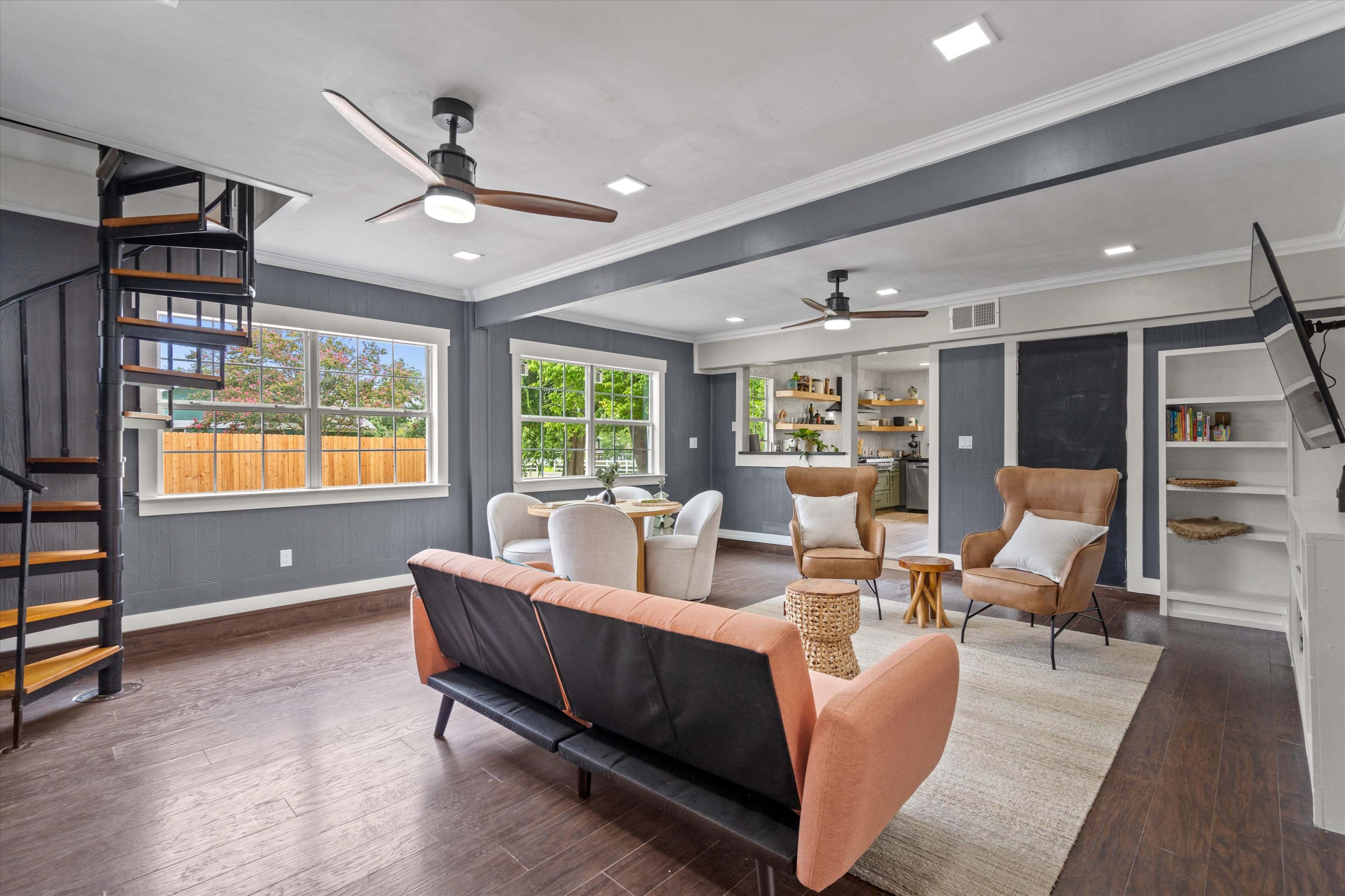 The image shows a modern living room with a spiral staircase, two ceiling fans, and a combination of seating options including a couch and armchairs.
