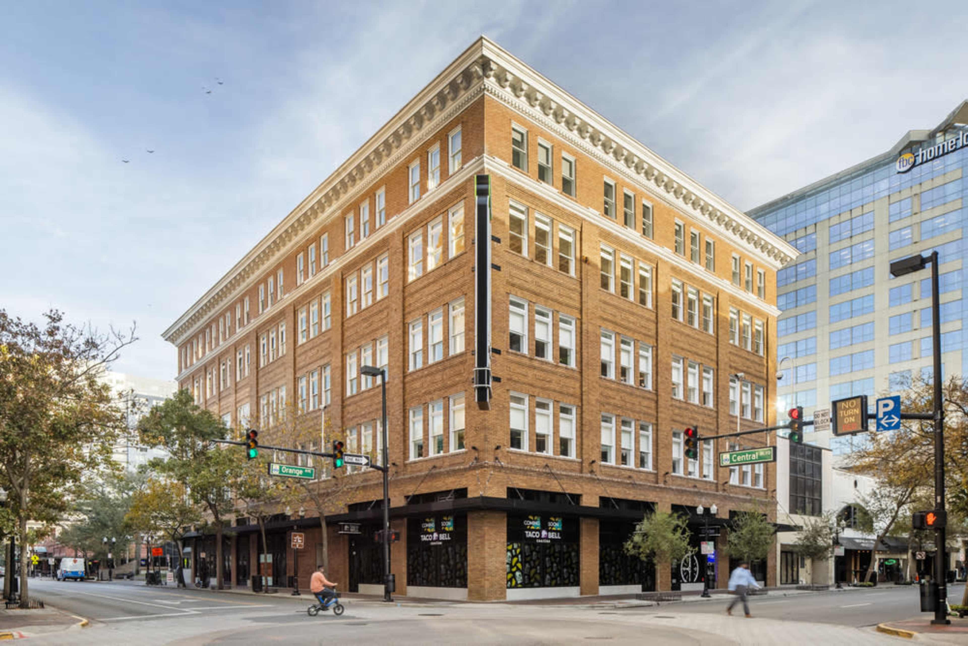 A large, brick four-story building at an intersection, with pedestrians and a cyclist nearby.