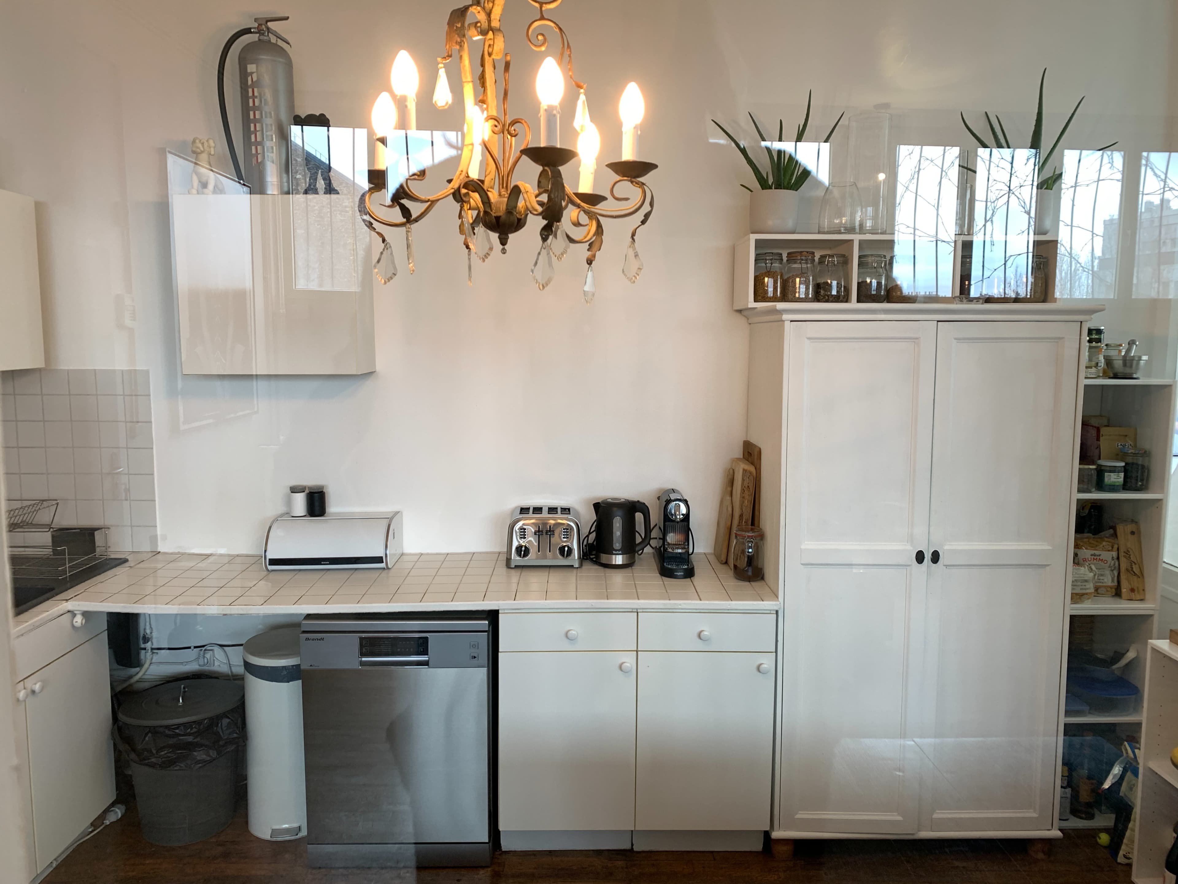A tidy kitchen with white cabinetry, a chandelier, and various appliances arranged on the countertops.