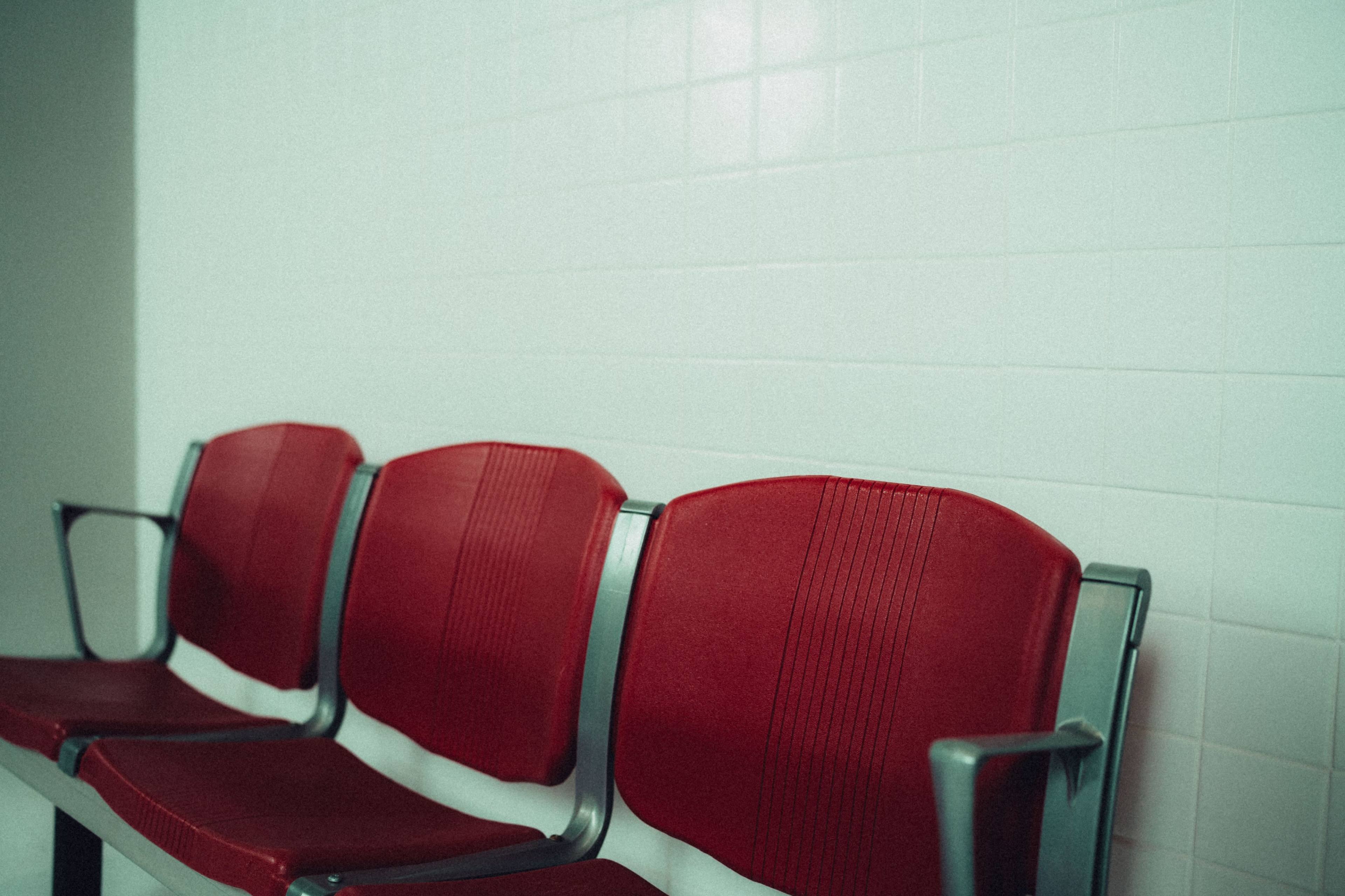 Three red chairs are aligned against a light-colored tiled wall.
