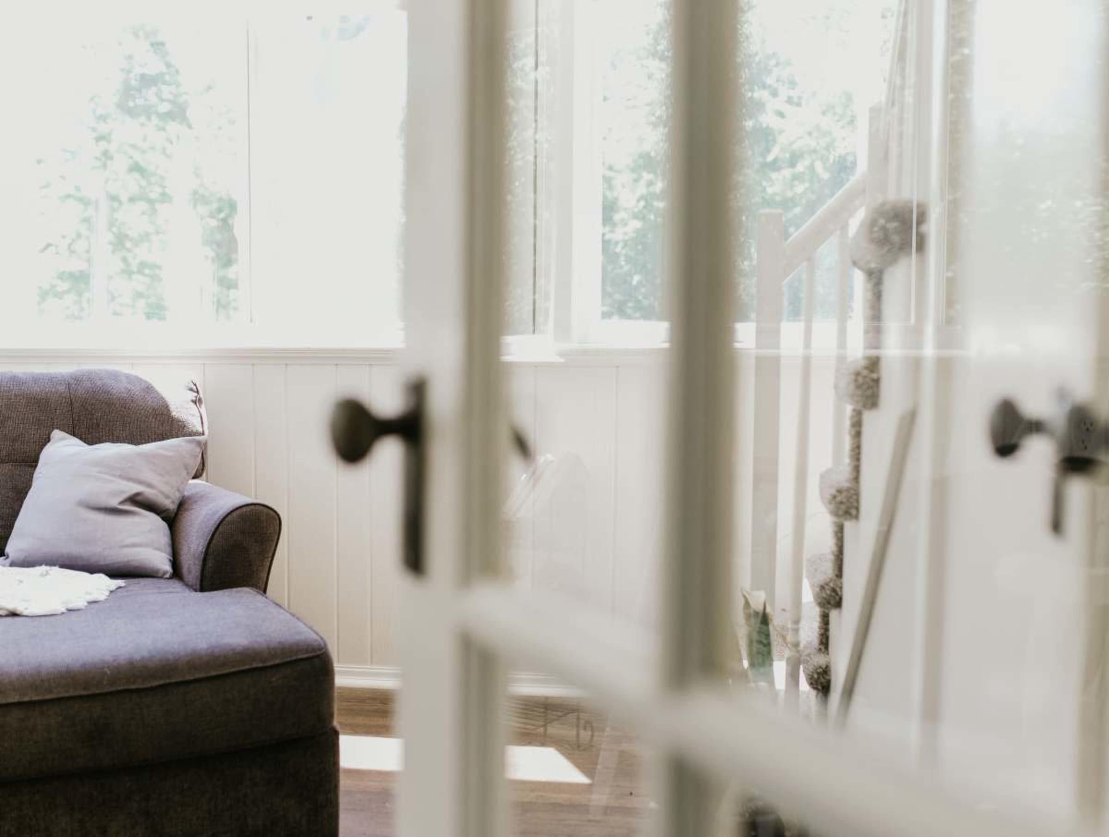 A cozy living room is visible through a glass-paneled door, featuring a dark sofa and a staircase in the background.