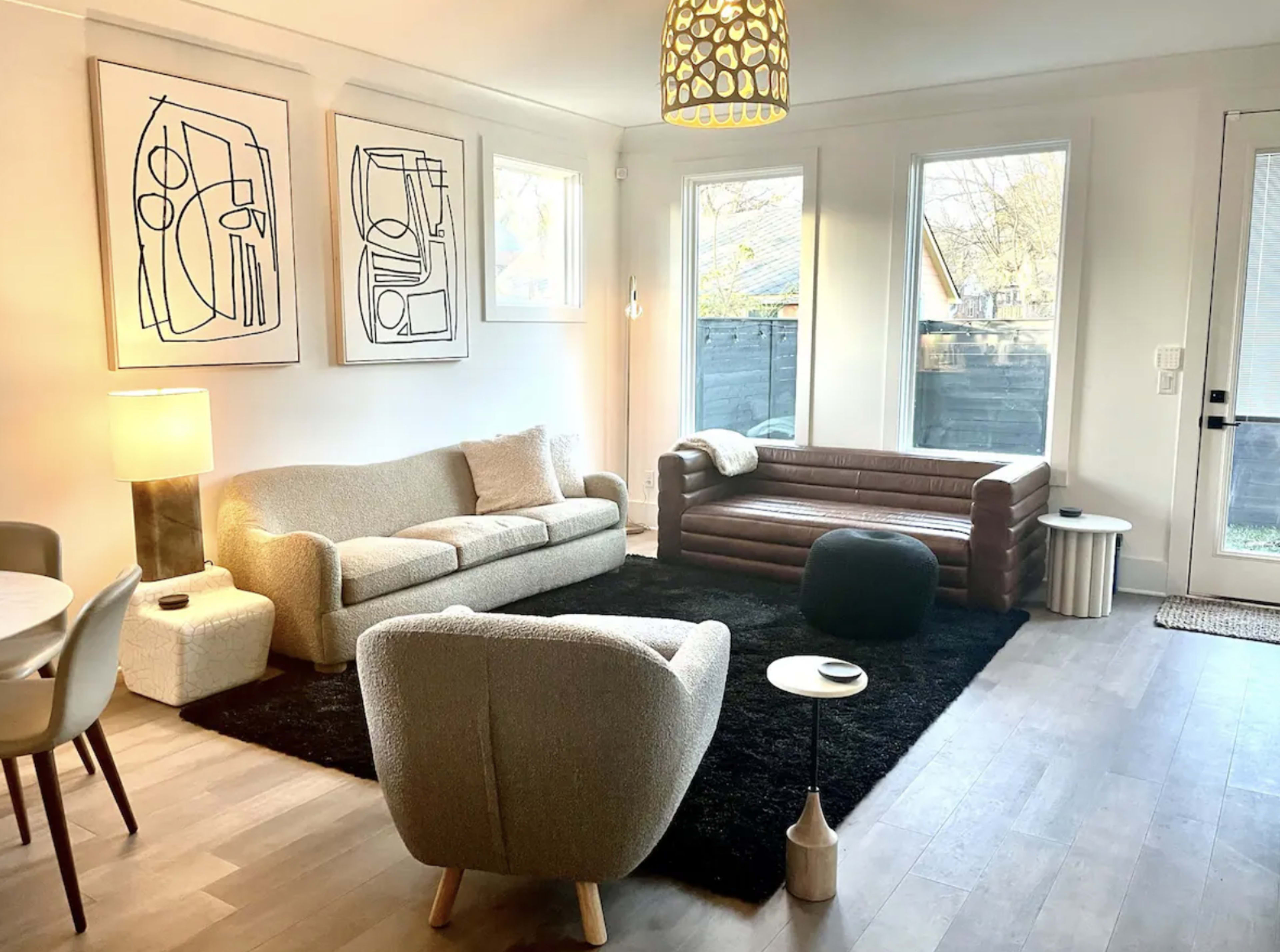 A modern living room featuring two sofas, a round coffee table, a floor lamp, and large windows allowing natural light to fill the space.