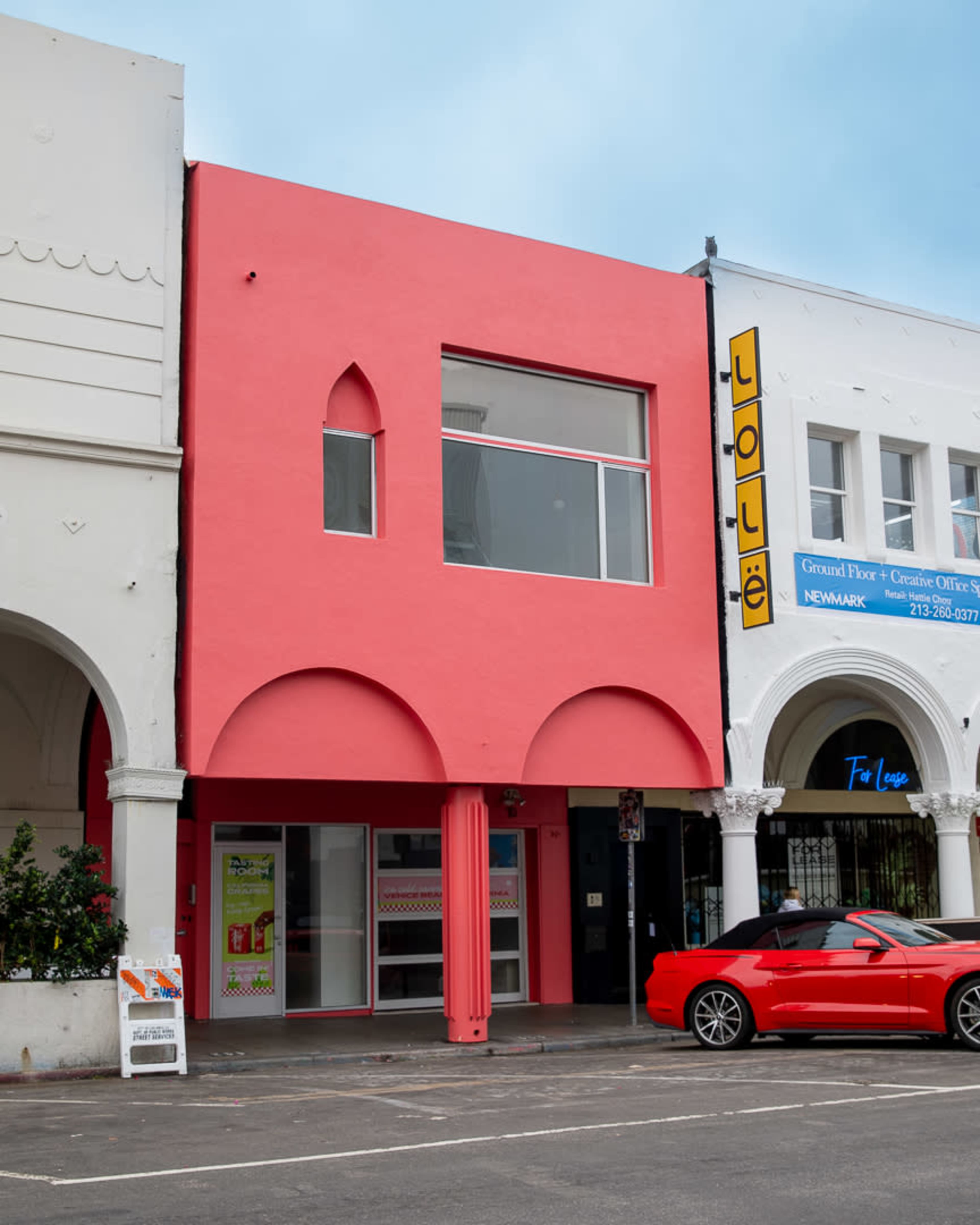 A two-story building with a bright pink facade and arched windows, located next to a white building with a yellow sign.