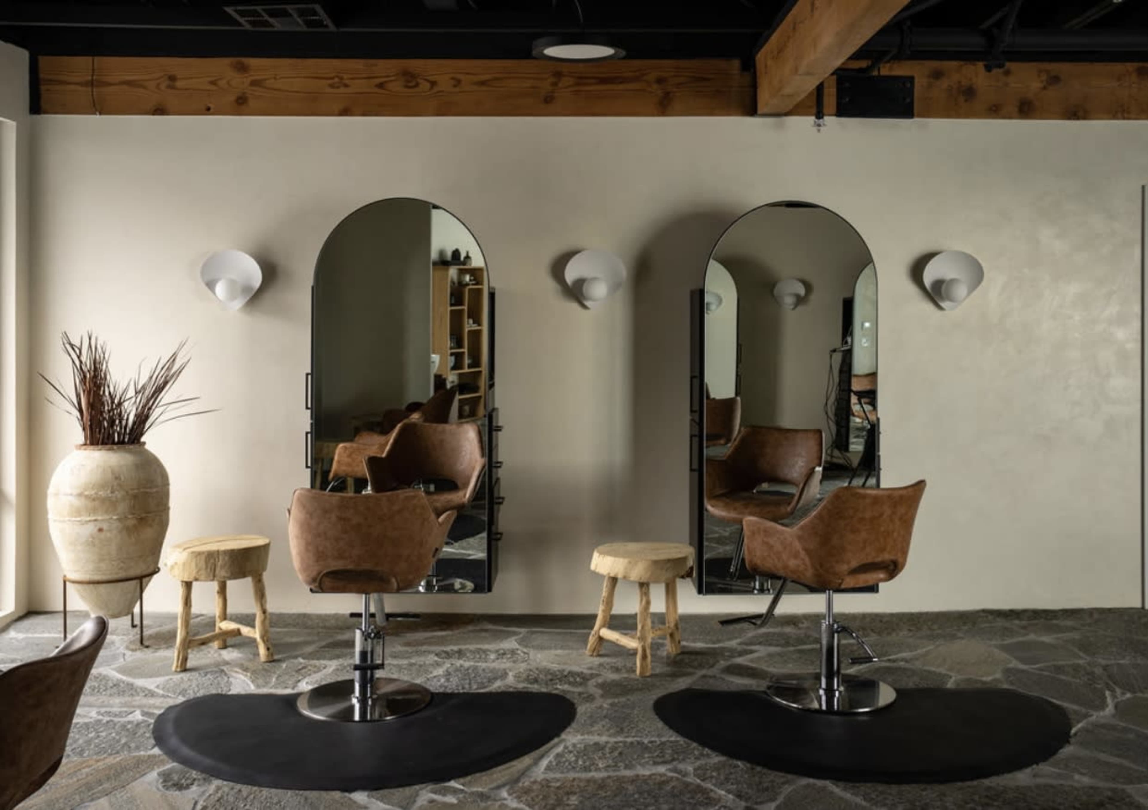 A minimalist hair salon with two styling chairs, mirrors, and decorative elements on a stone floor.