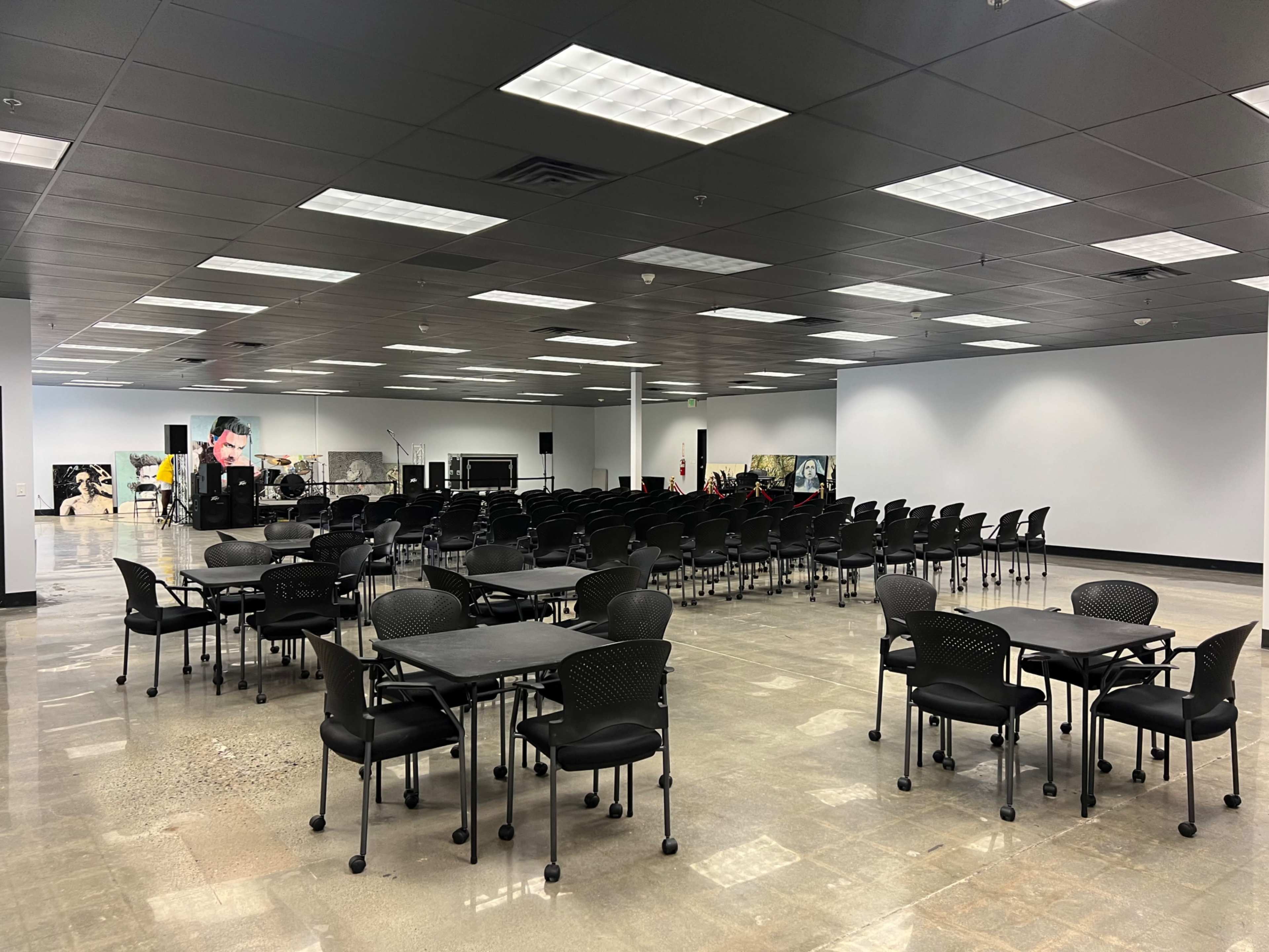 A spacious room filled with rows of black chairs and tables arranged for a gathering.