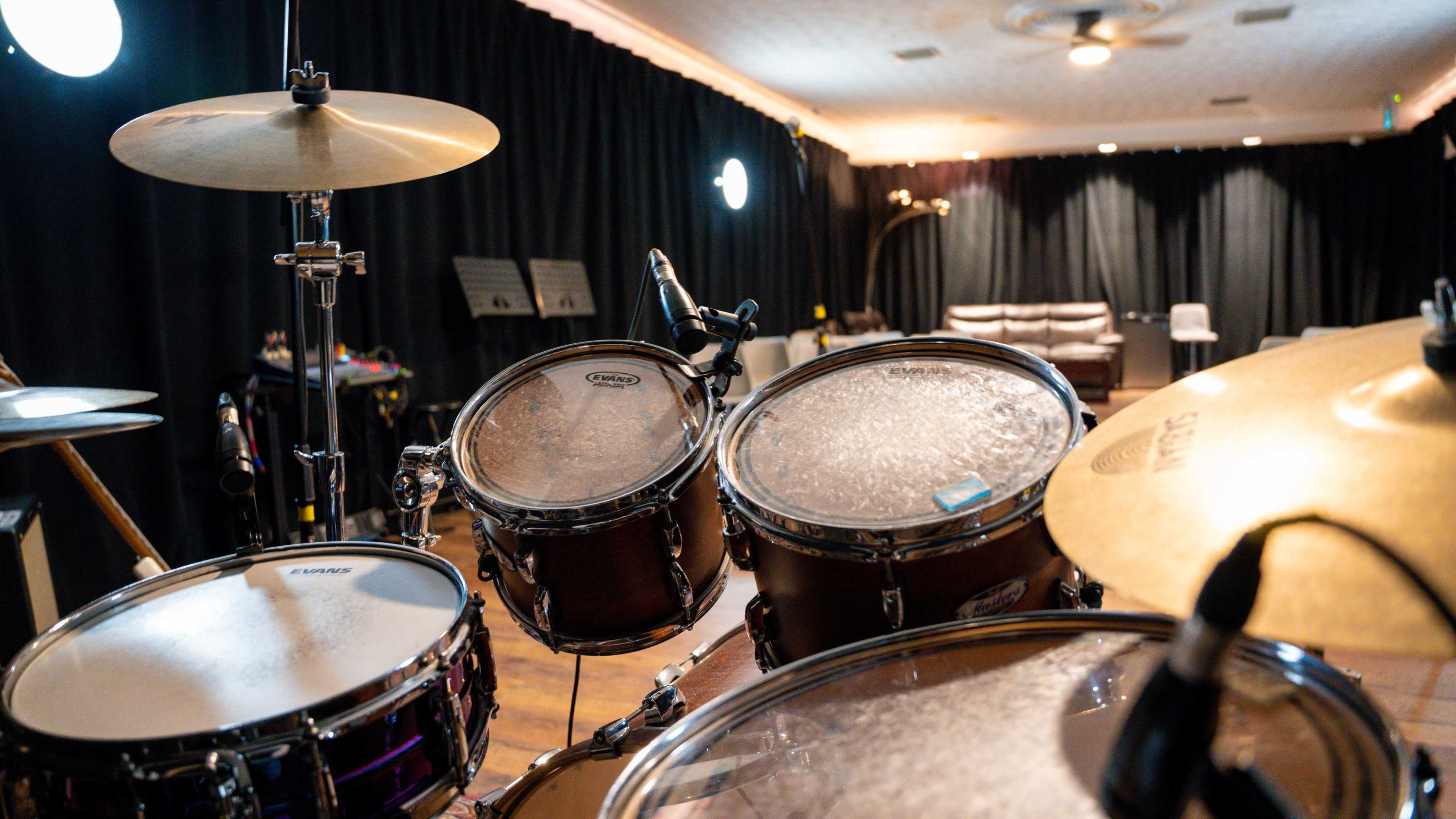 A well-equipped music studio with a drum set in the foreground and a seating area in the background.