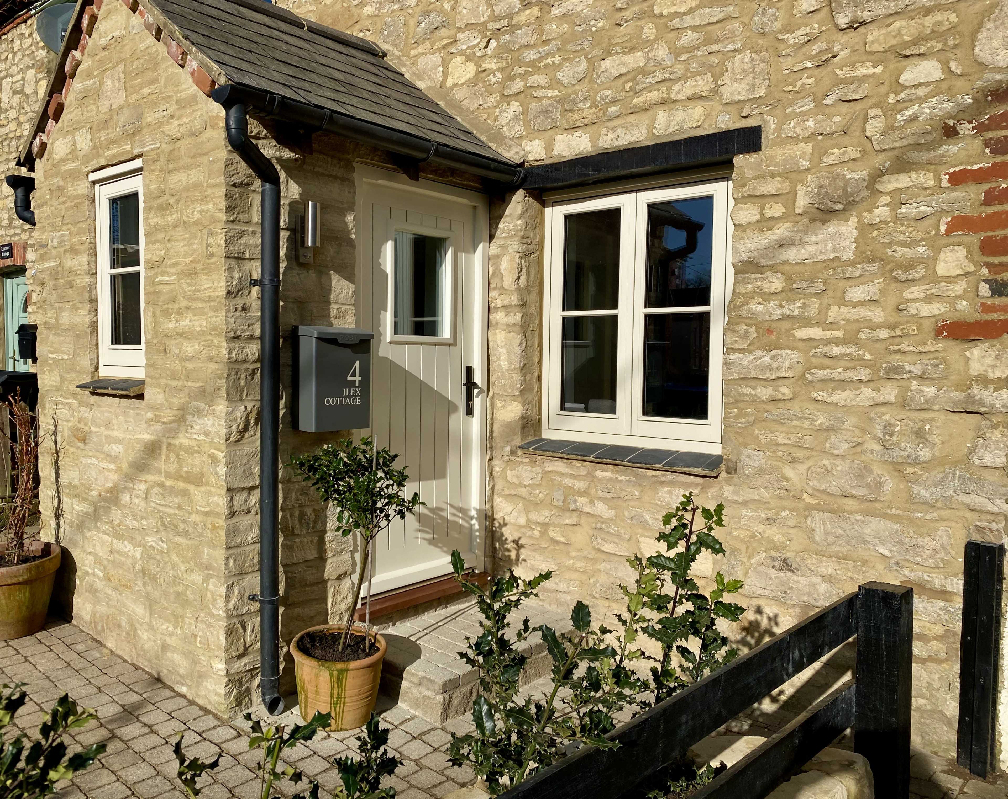 The entrance of a stone cottage with a white door, a planter, and a house number displayed on a dark sign.