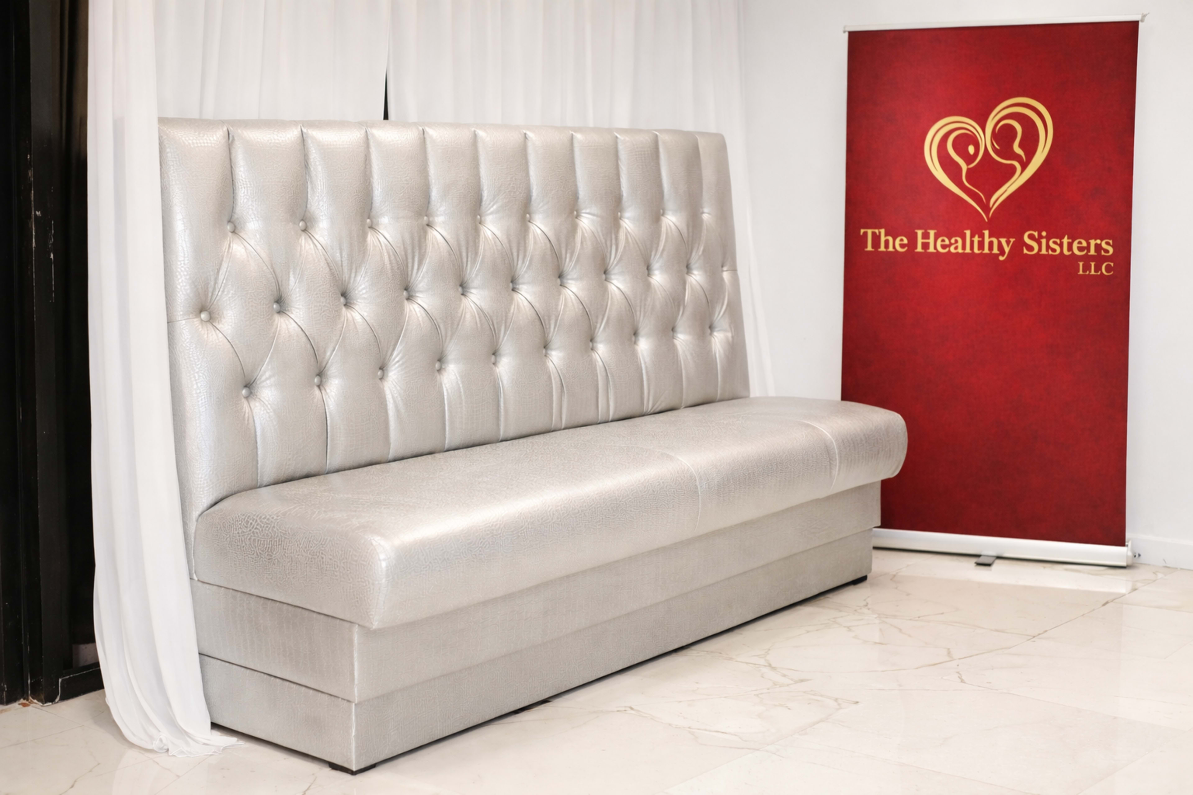 The image shows a silver tufted bench against a white backdrop, with a red banner beside it featuring the text "The Healthy Sisters LLC."