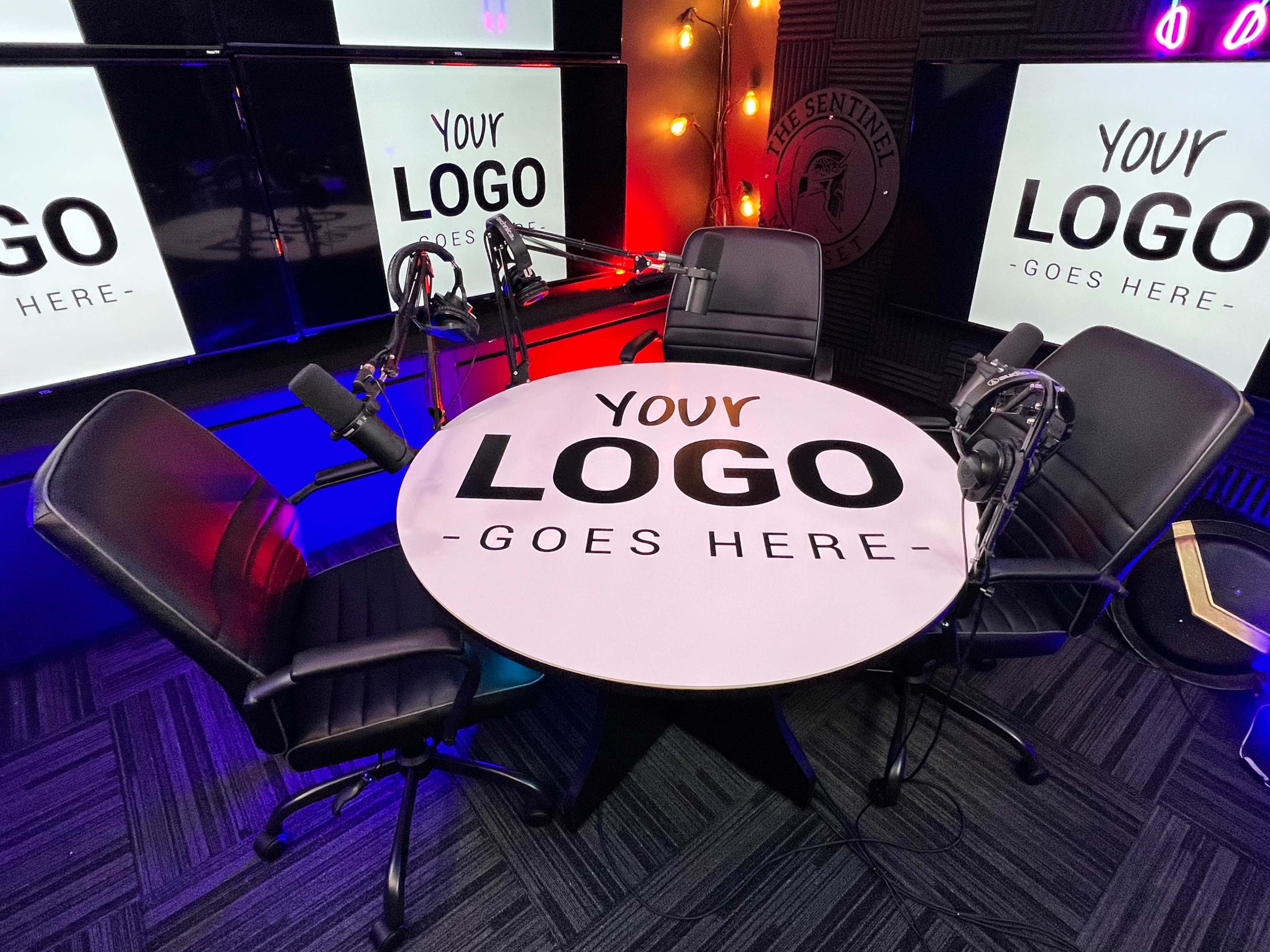 A round table with microphones and three black chairs is set up in a studio labeled "Your Logo Goes Here."
