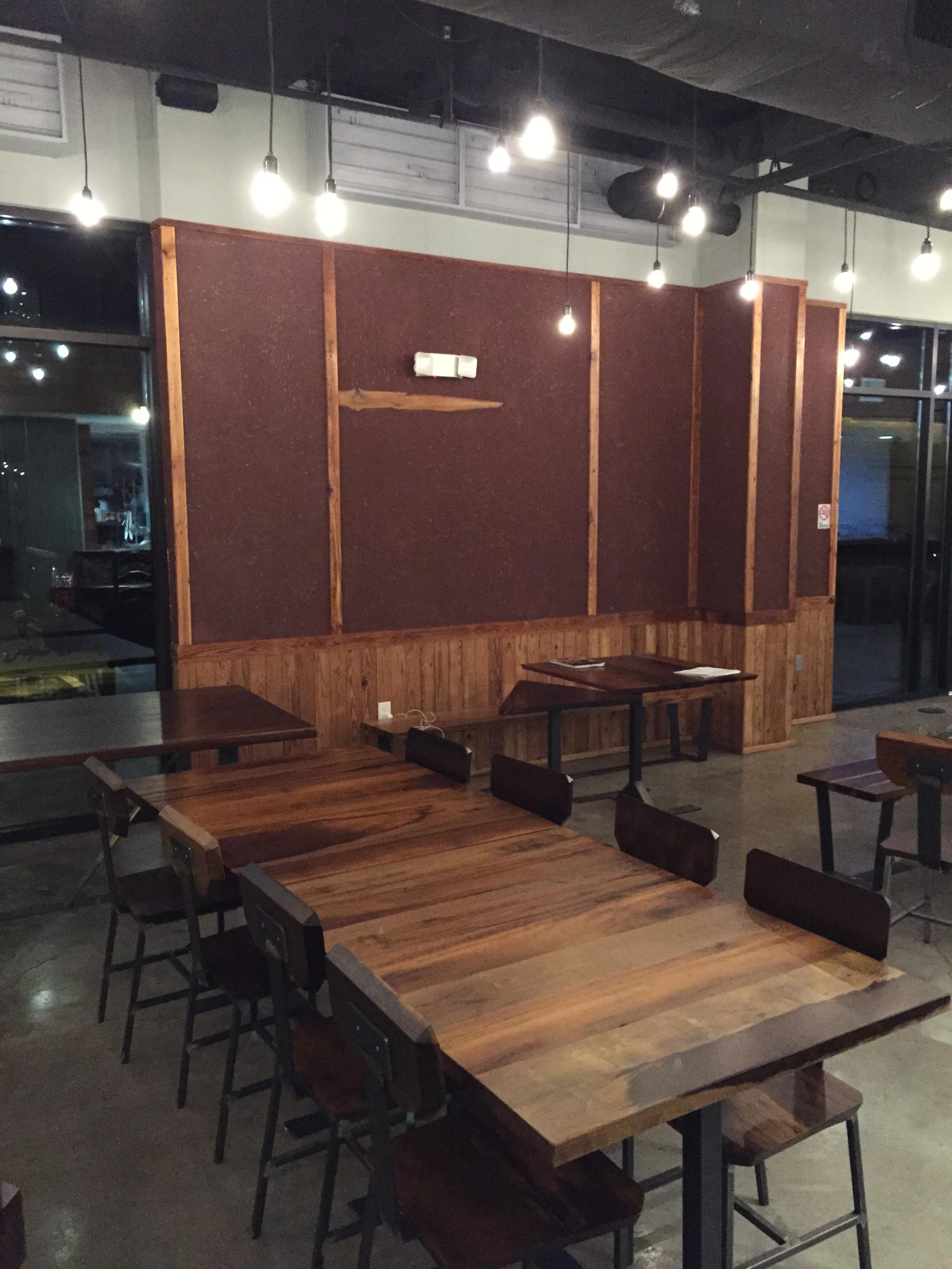 The image shows a dimly lit cafe interior featuring wooden tables and a textured wall with pendant lights hanging from the ceiling.