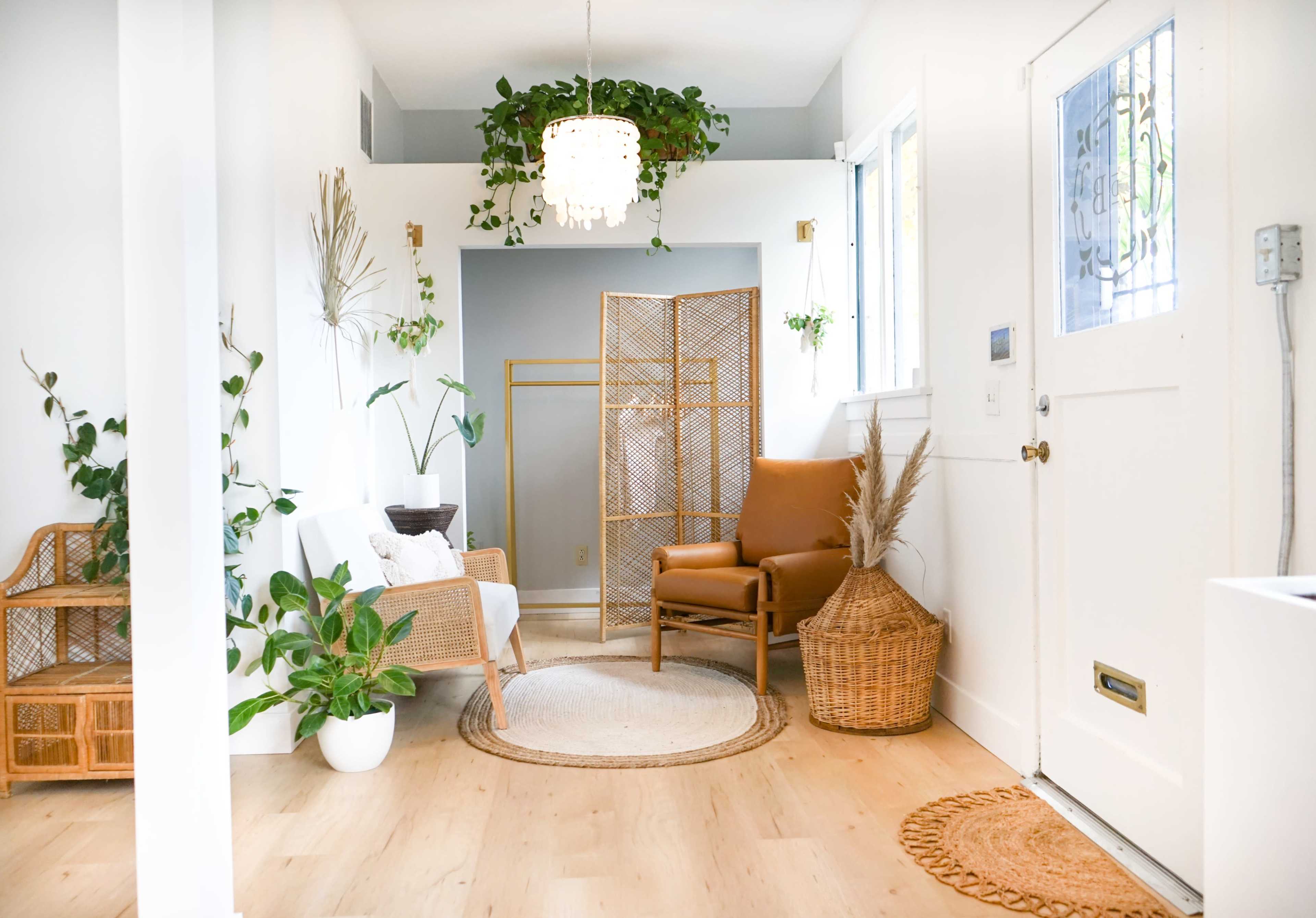 A light-filled entryway with a rattan chair, a white sofa, indoor plants, a round rug, and a door leading outside.