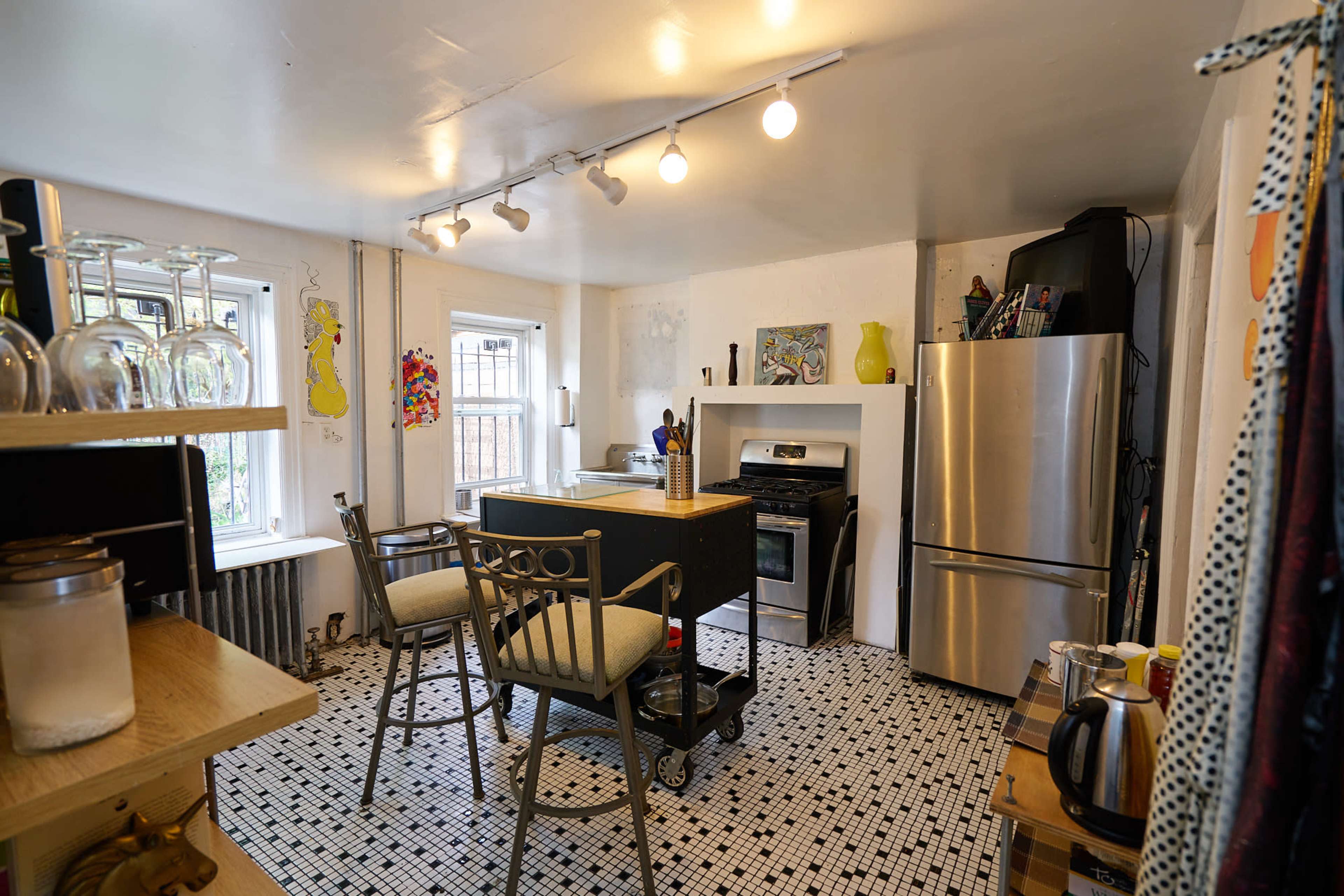 The image shows a modern kitchen with a small island, stainless steel appliances, and a black and white tiled floor.