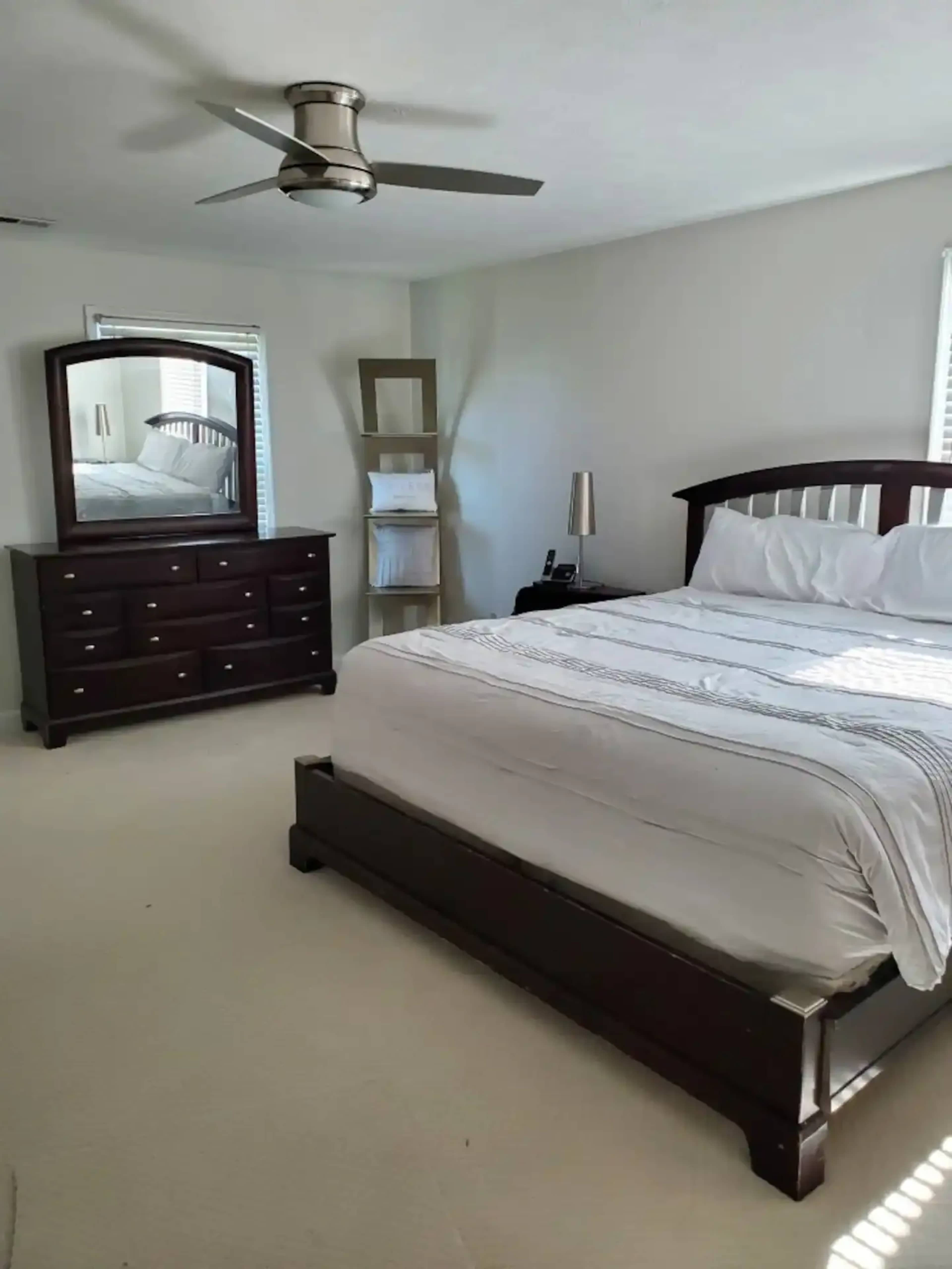 A bedroom with a bed, a dresser, a mirror, a lamp, and a bookshelf arranged in a well-lit space.