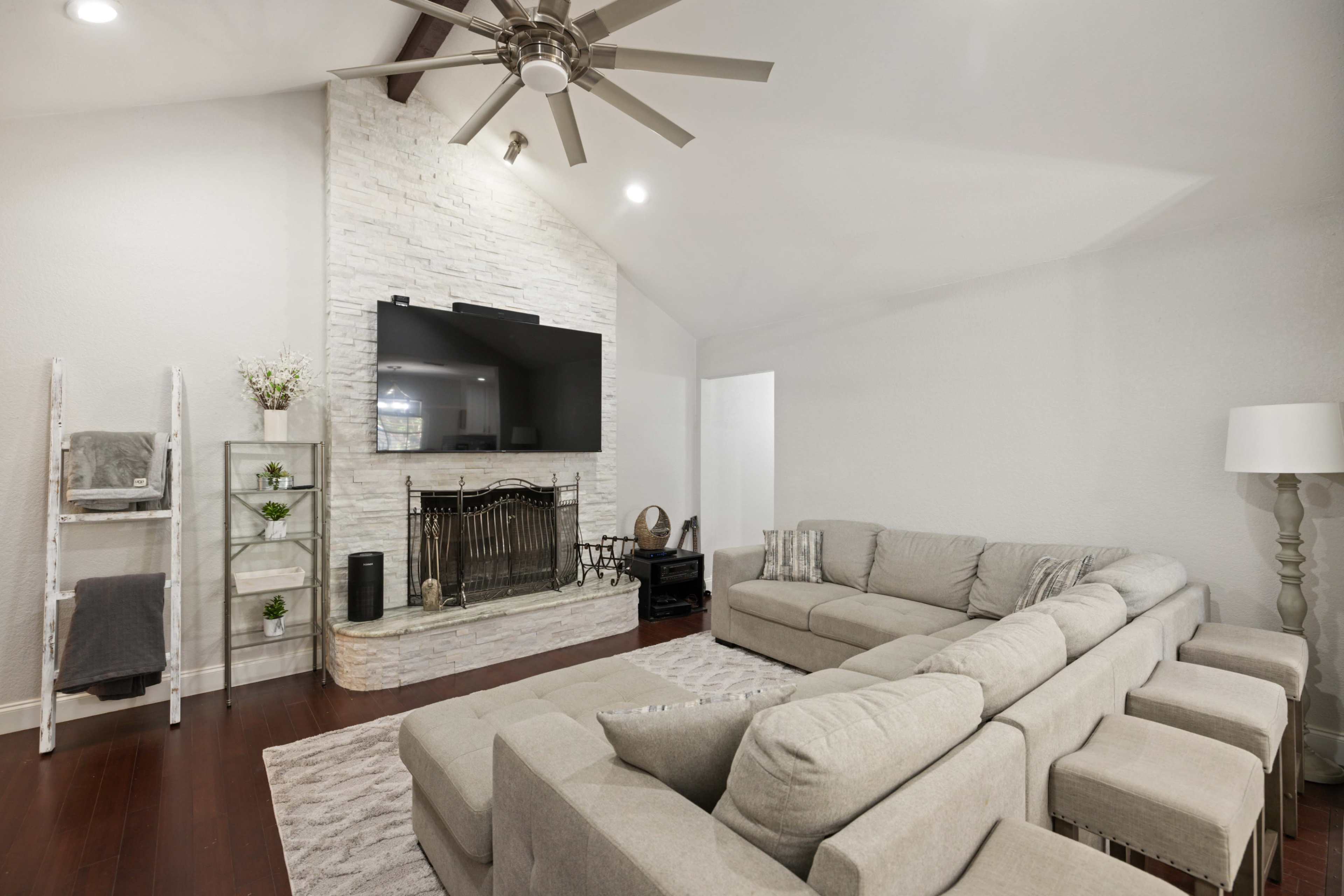 The living room features a spacious sectional couch facing a stone fireplace with a mounted flat-screen TV above it.