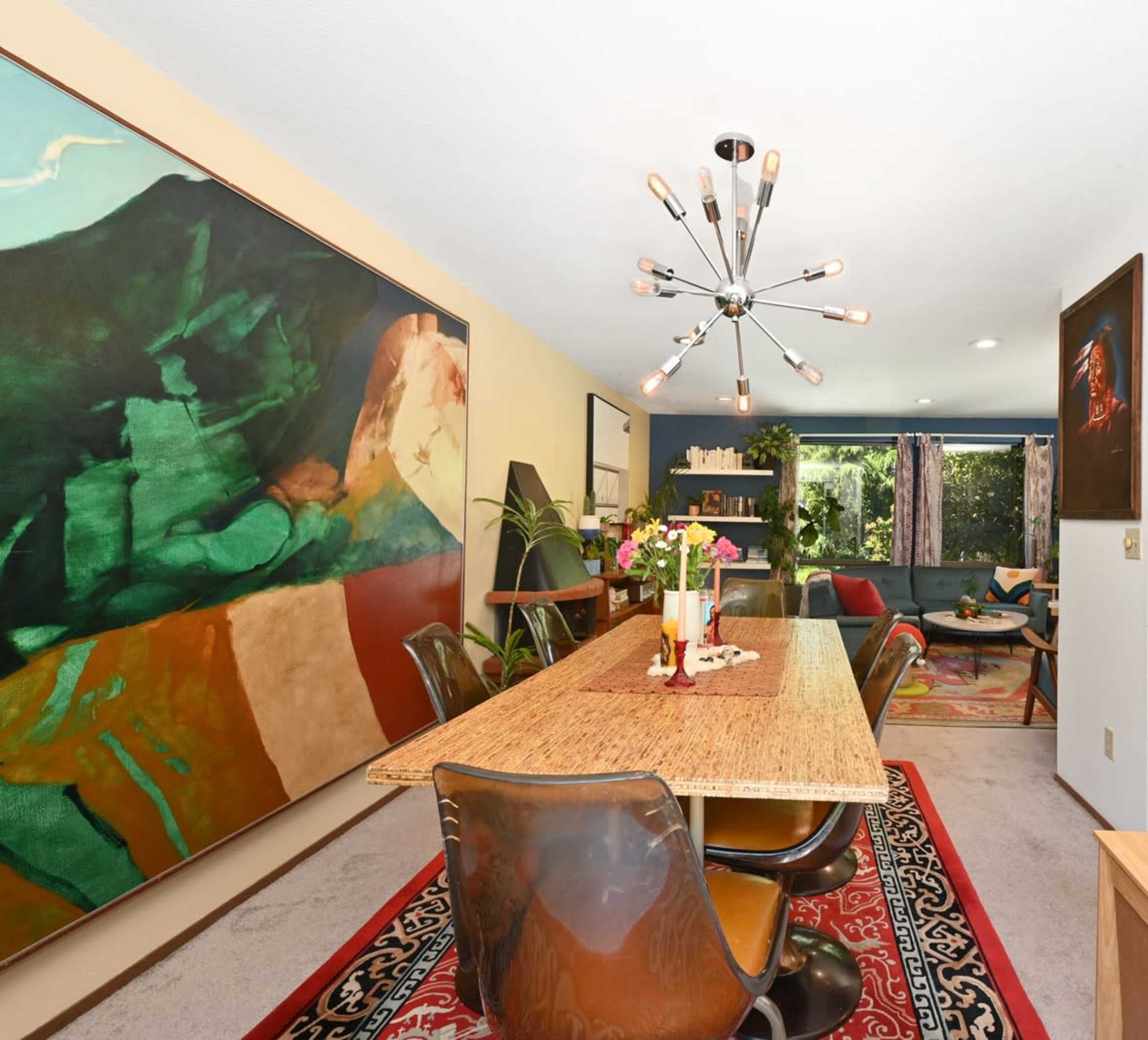 A spacious dining area features a long wooden table surrounded by black chairs, with large abstract paintings on the walls.