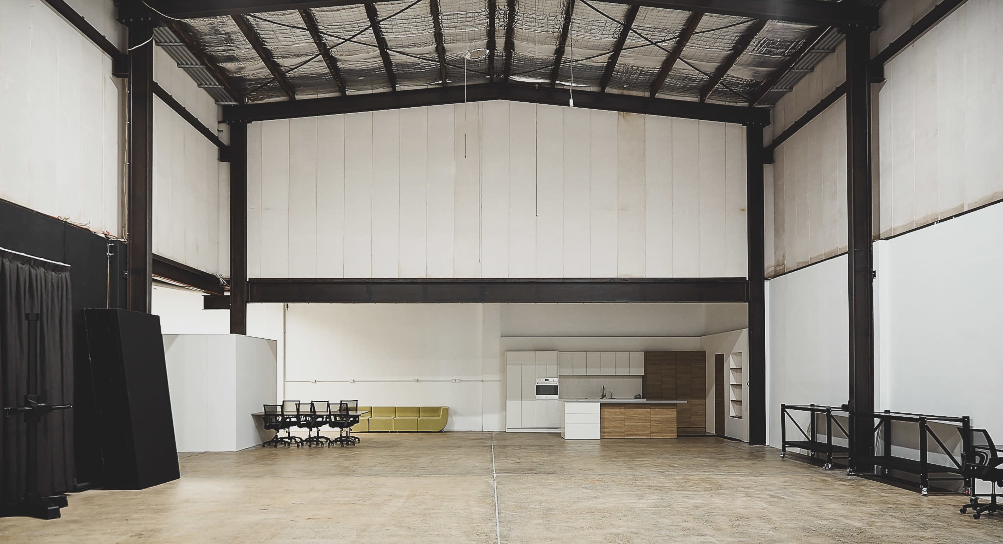 A spacious industrial room with high ceilings, featuring a kitchenette and seating area along one side.