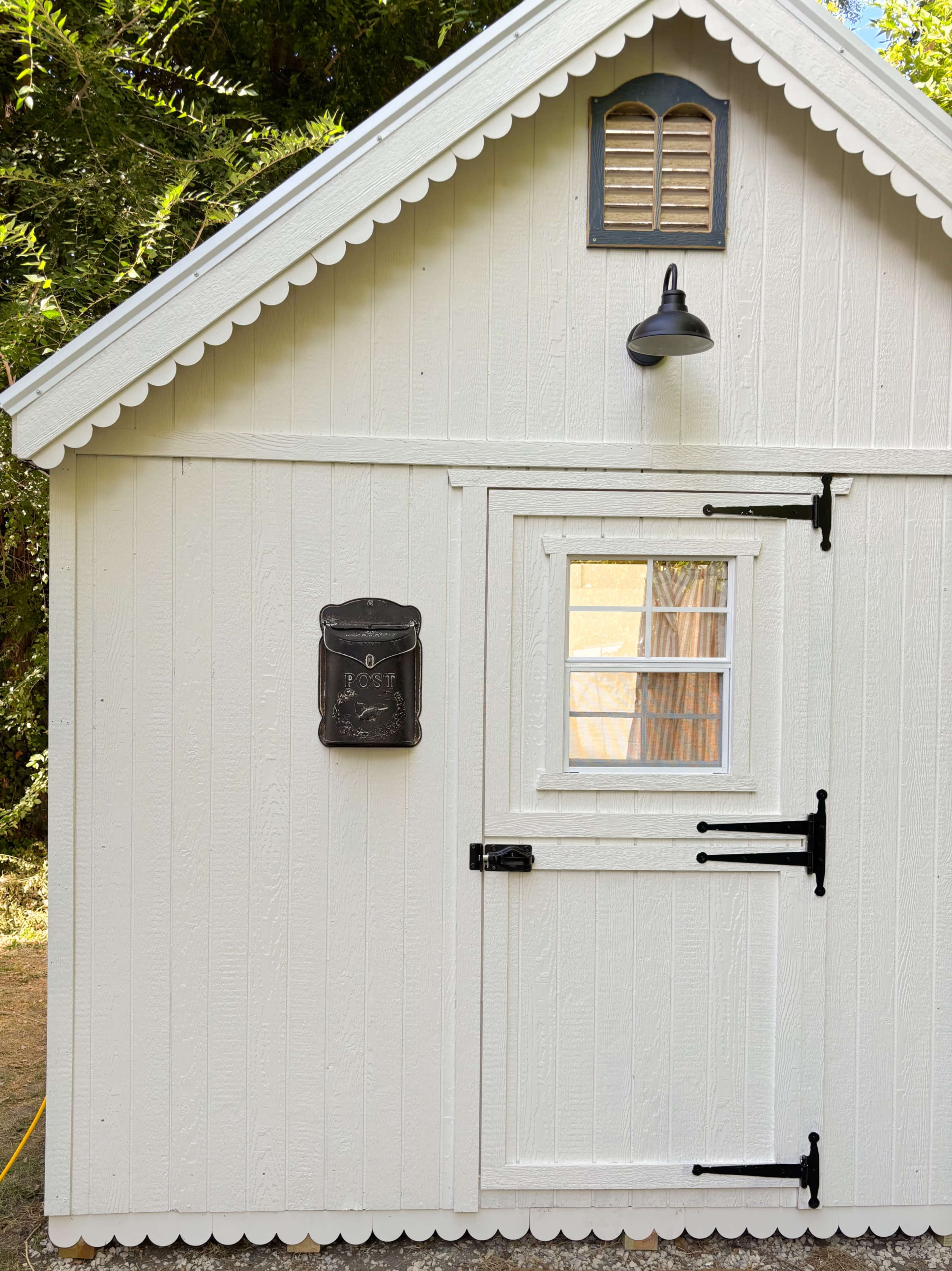 The image shows a small white wooden building with a door, a window, and a decorative roof.