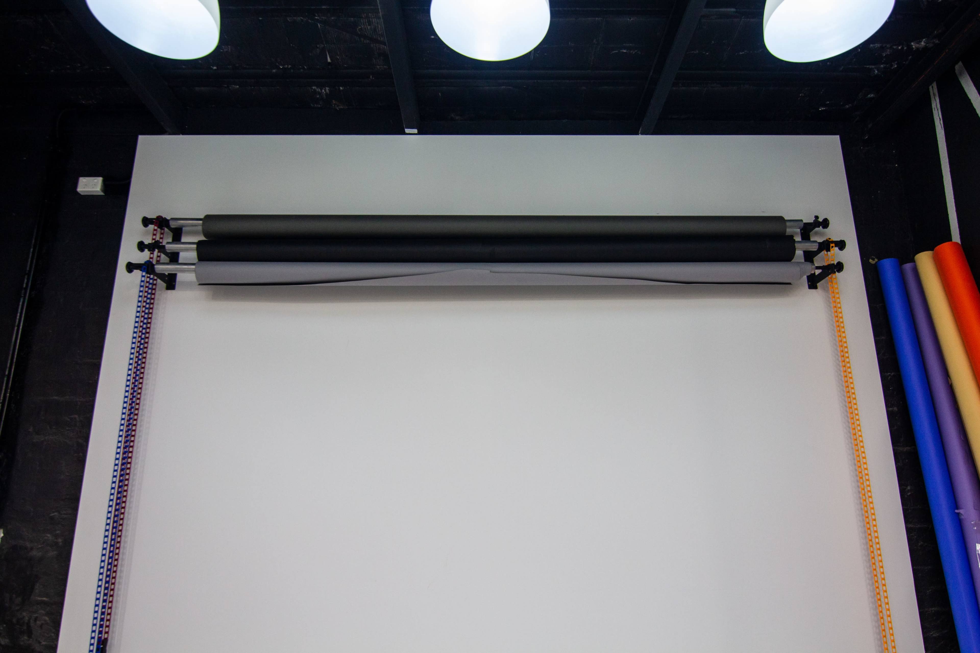 A wall with three rolled backgrounds mounted on a horizontal bar, surrounded by several vertical color rolls.