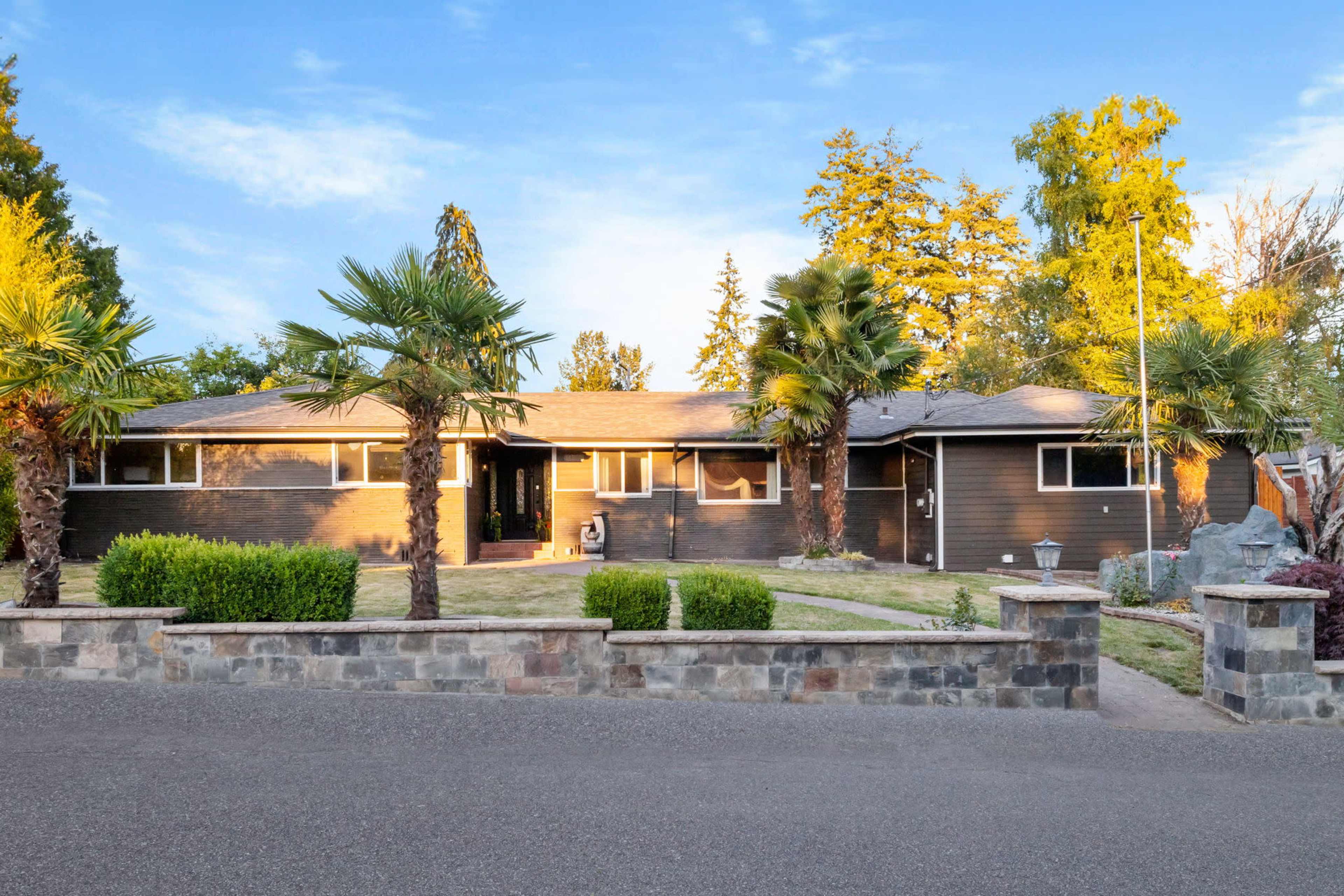 A single-story house with a landscaped front yard and palm trees sits on a quiet street.