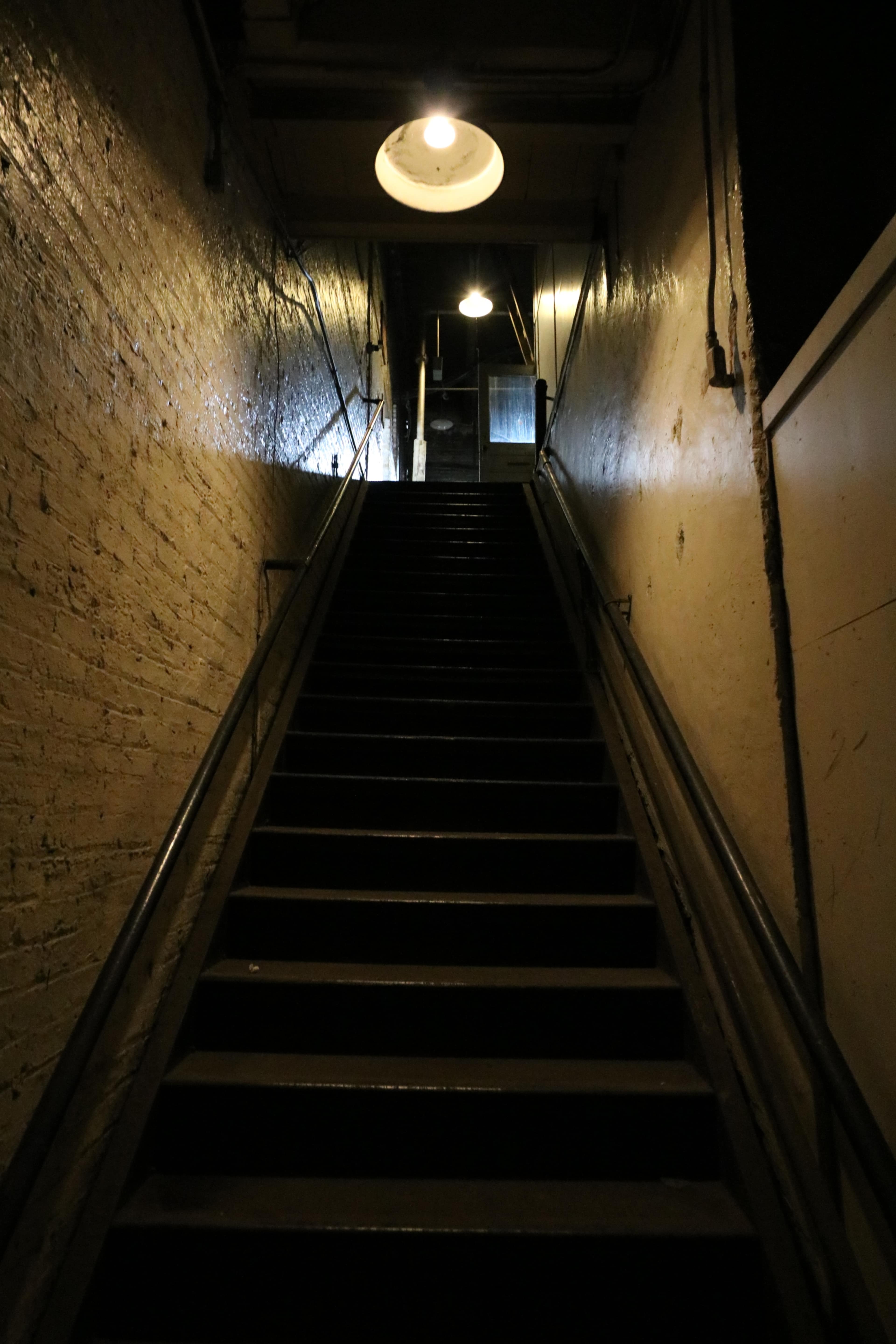 A dimly lit staircase leads upward, illuminated by circular ceiling lights.