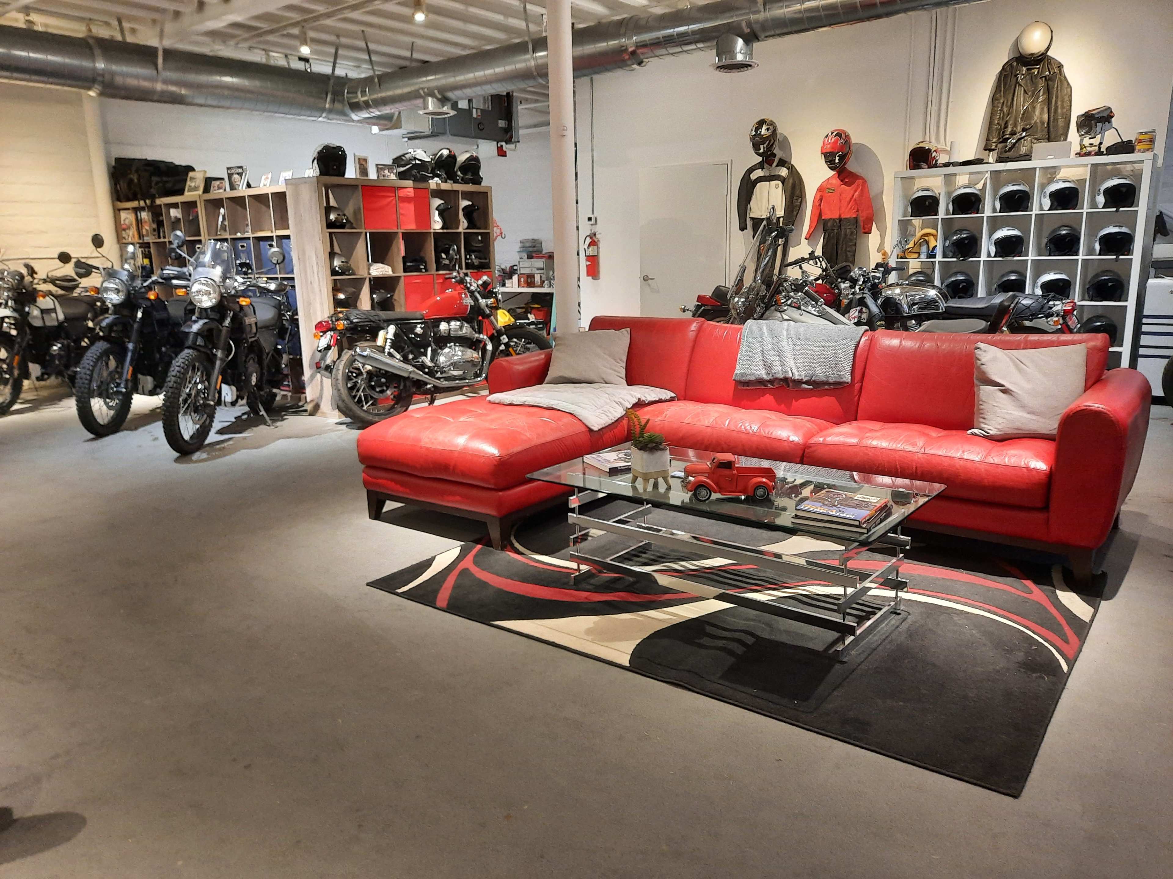 A spacious room with a red sectional sofa, glass coffee table, and shelves displaying motorcycles and helmets in the background.