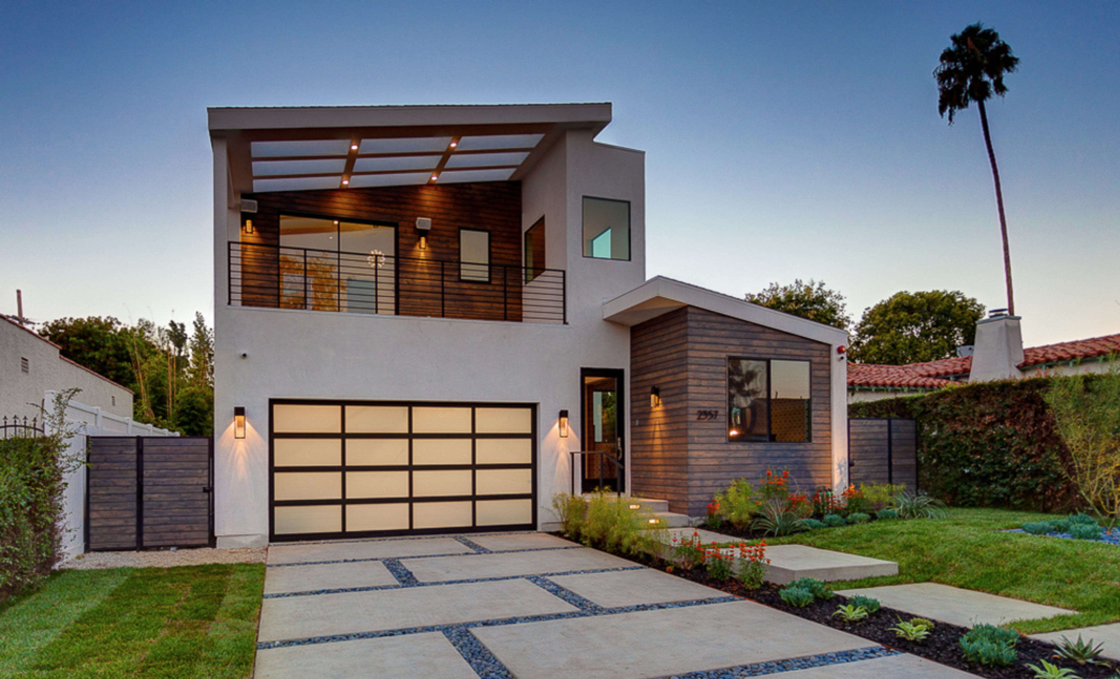 A modern two-story house with a sleek facade, a landscaped front yard, and a driveway leading to a garage.